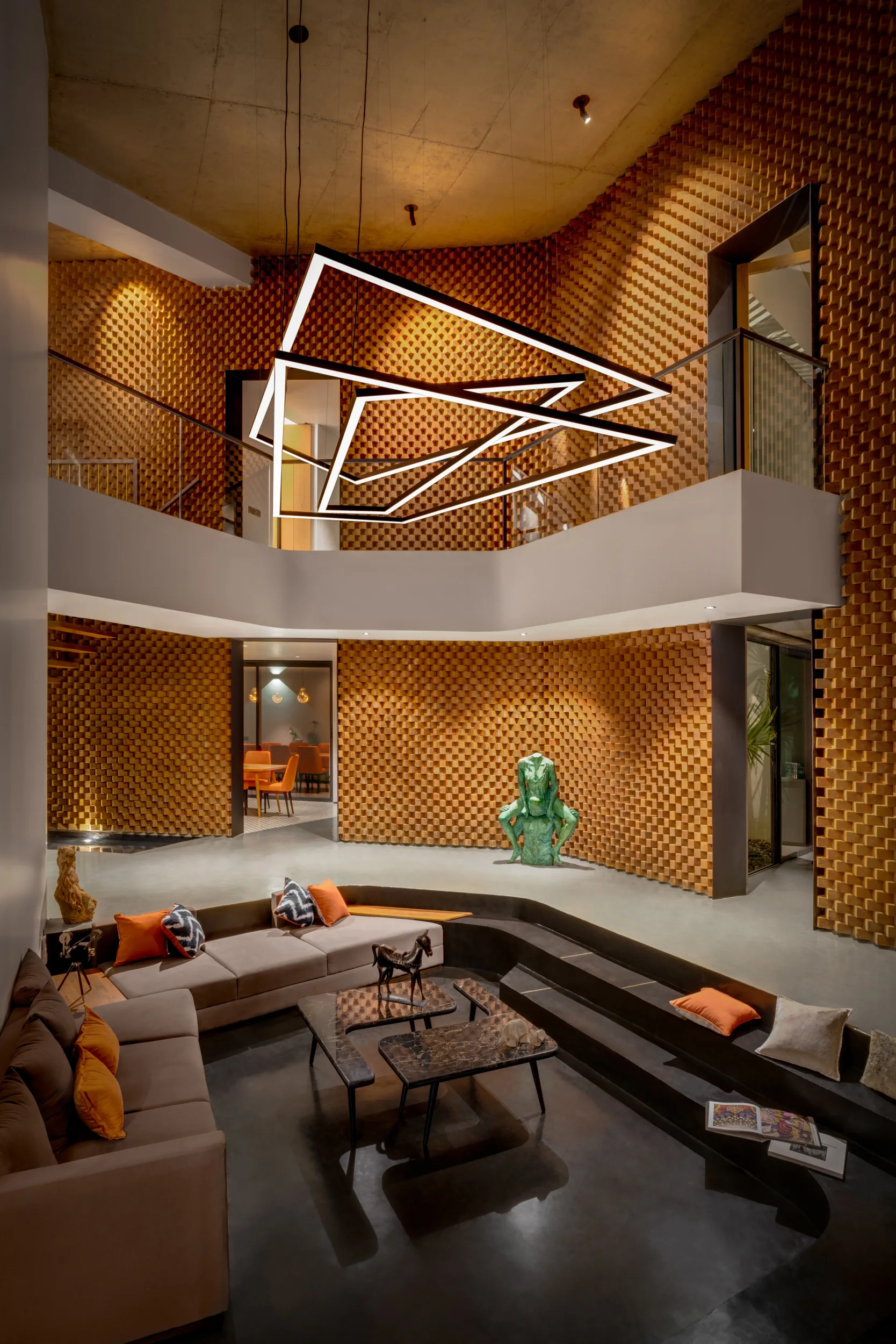 A multi-level living room features a sunken conversation pit with brown sofas, a large geometric LED chandelier, and textured 3D wood-block walls.