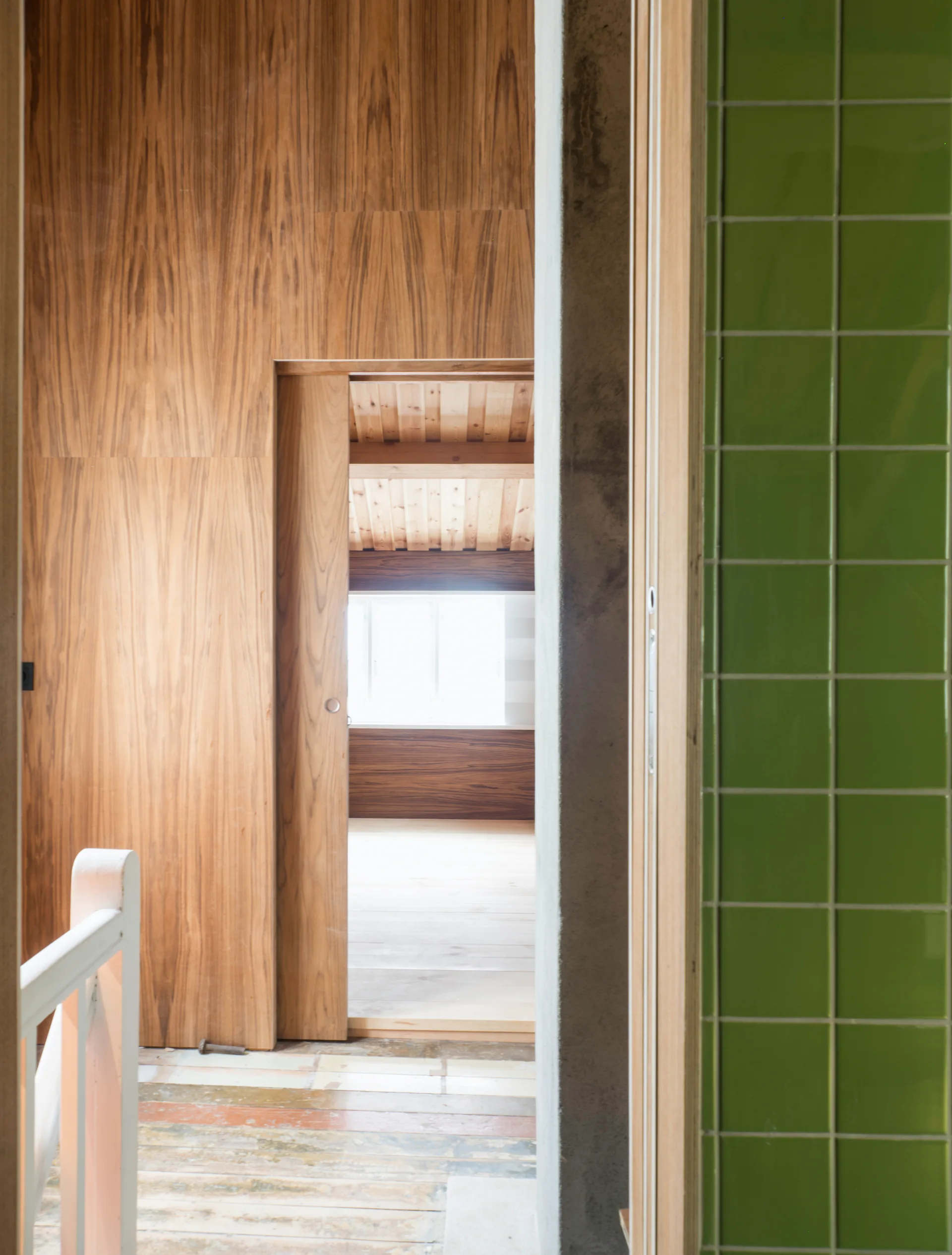 A hallway view looking through a wooden sliding door into a room with wood paneling and a wall of bright green square tiles.