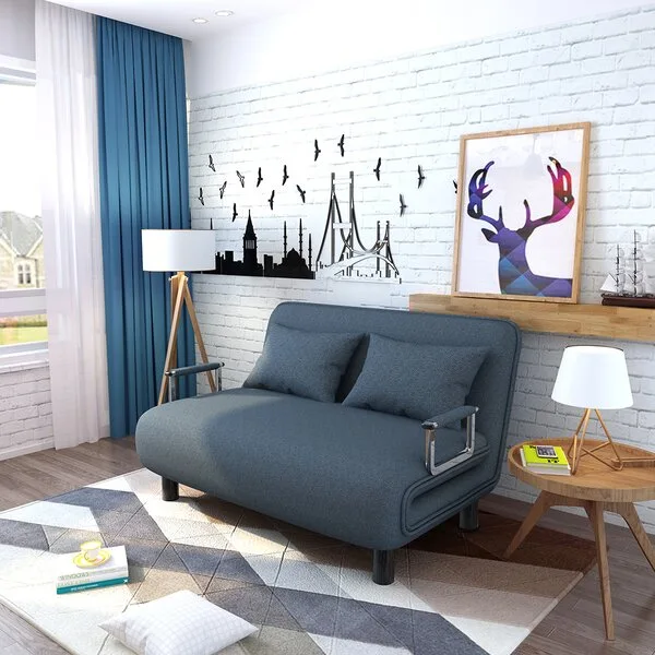 A blue upholstered sleeper sofa sits on a geometric rug in front of a white painted brick wall decorated with a cityscape decal.