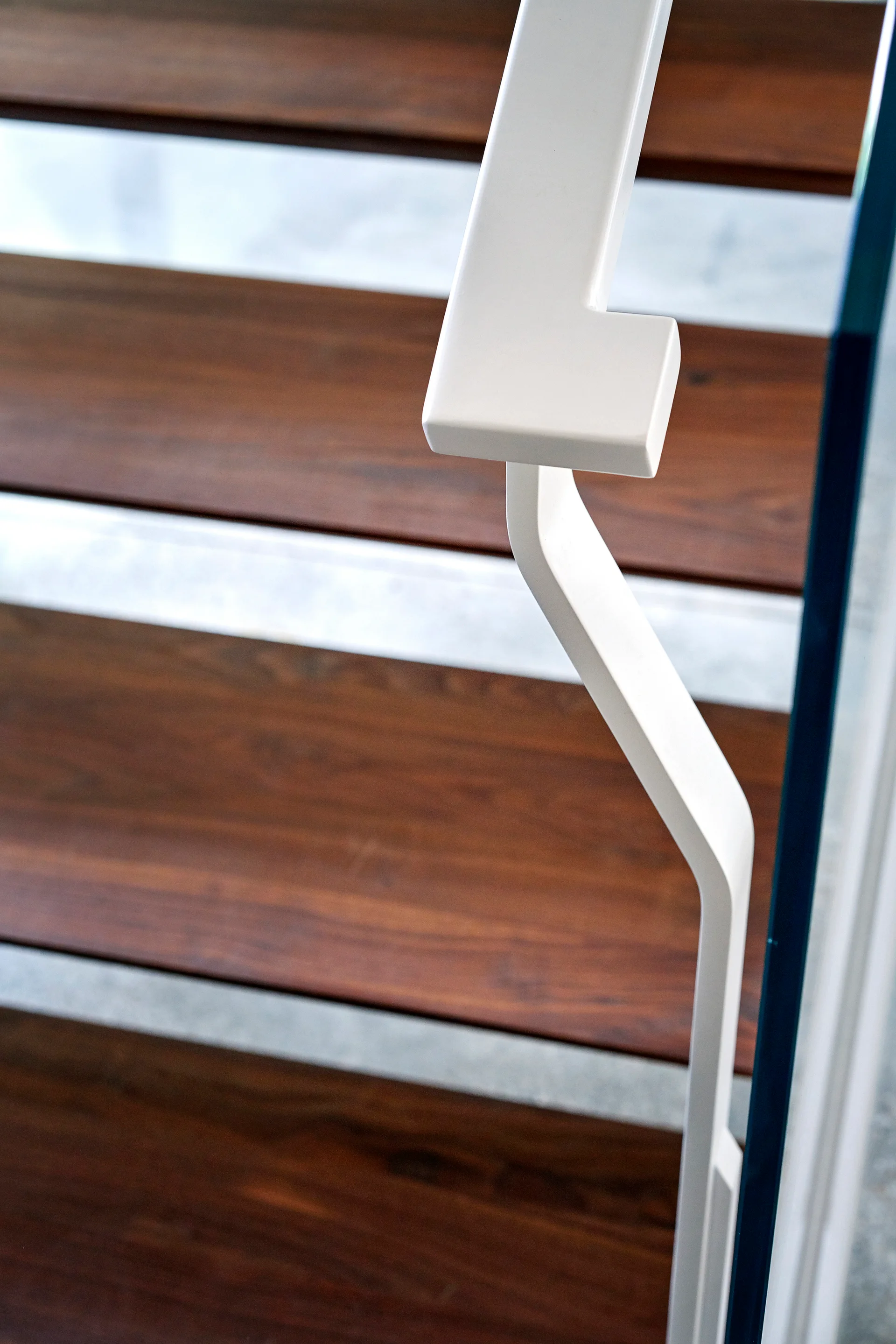 A close-up view of a minimalist staircase featuring dark brown wooden treads and a smooth white metal handrail.