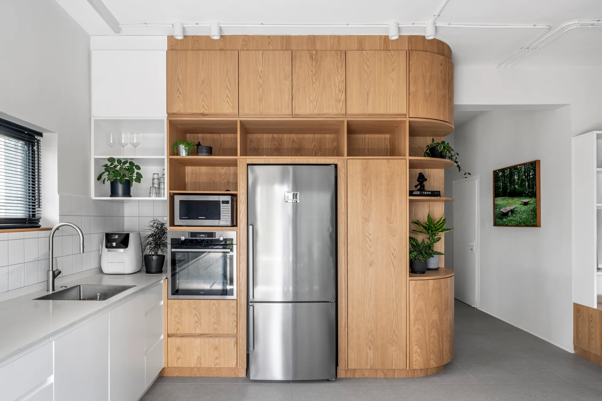 A modern kitchen featuring tall wood-toned cabinetry with curved corner shelving, built-in stainless steel appliances, and white lower cabinets.