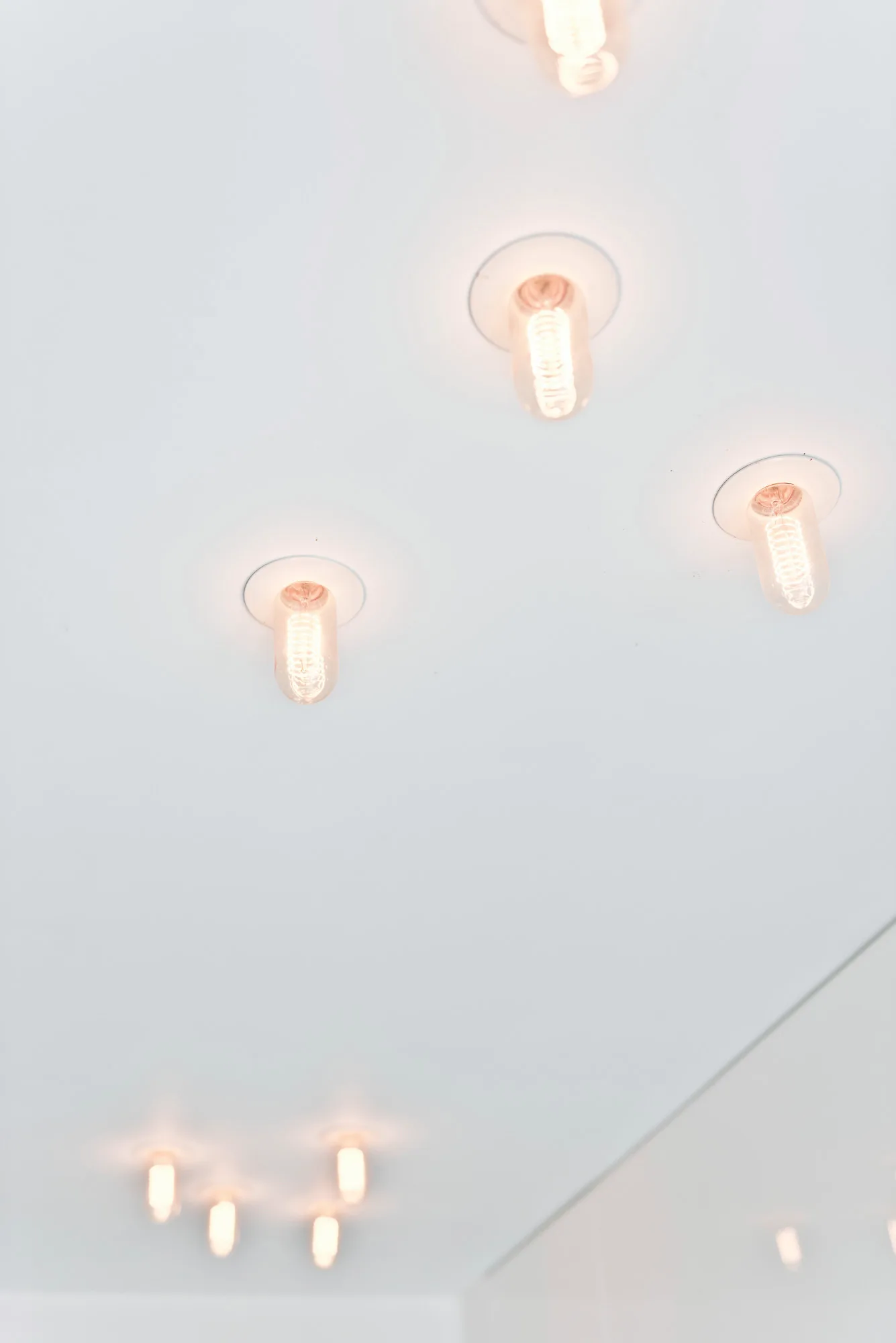 Multiple recessed light fixtures with glowing, warm-toned filament bulbs are set into a smooth white ceiling.