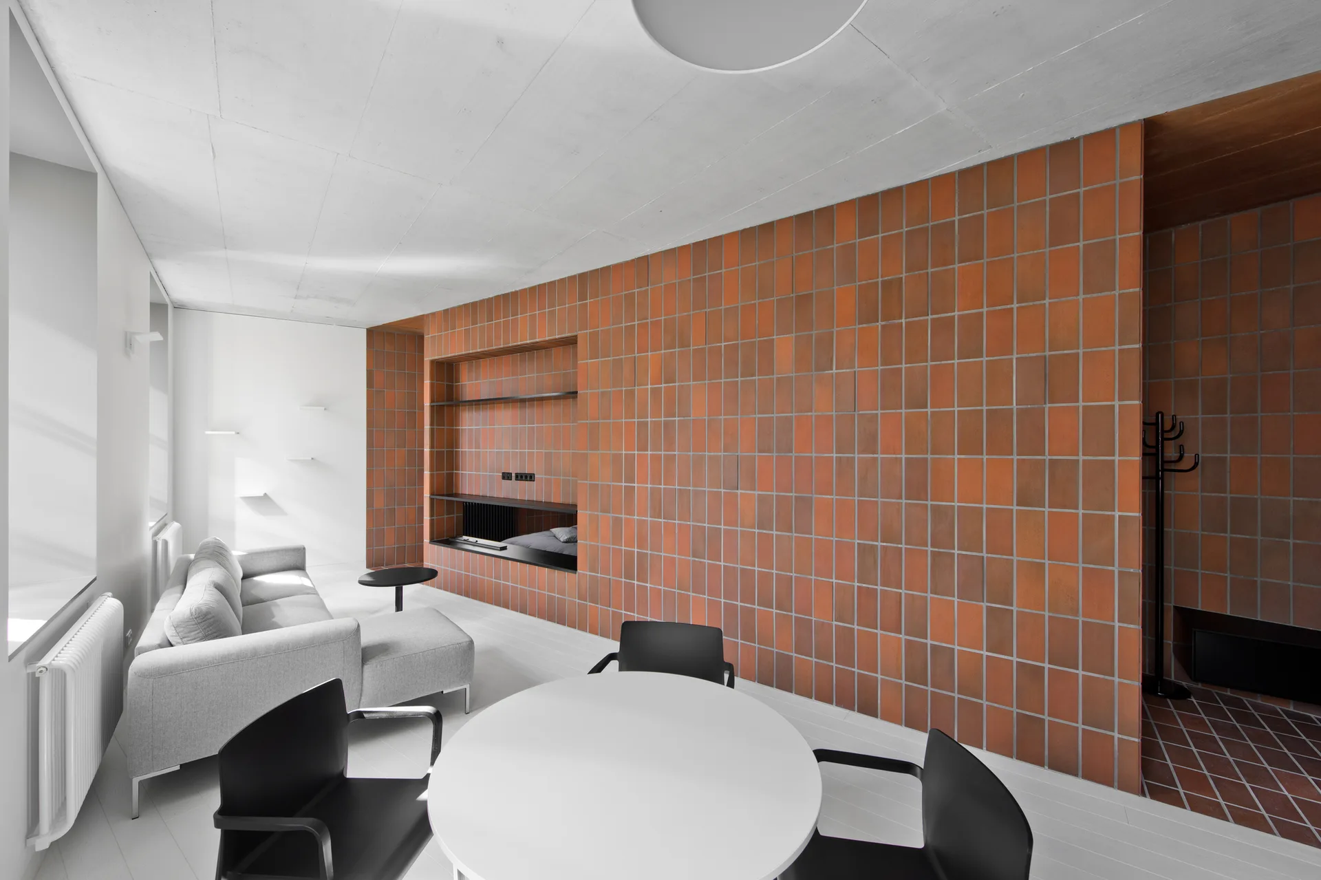 A modern open-plan living and dining space featuring a light grey sectional sofa and a large orange terracotta-tiled feature wall.
