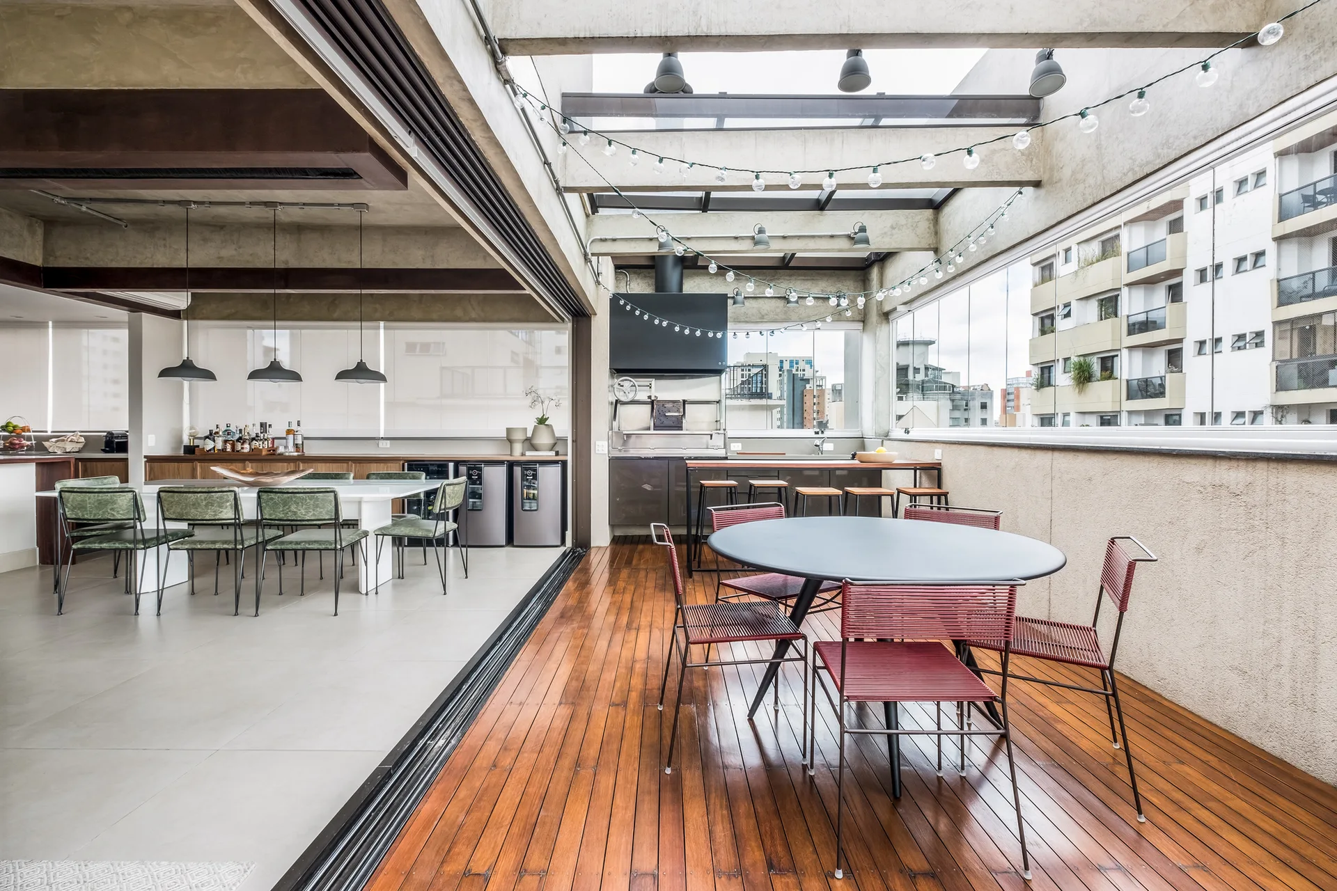 An open-concept dining area transition to an outdoor terrace featuring wood plank decking, a circular table with red chairs, and an outdoor grill station.