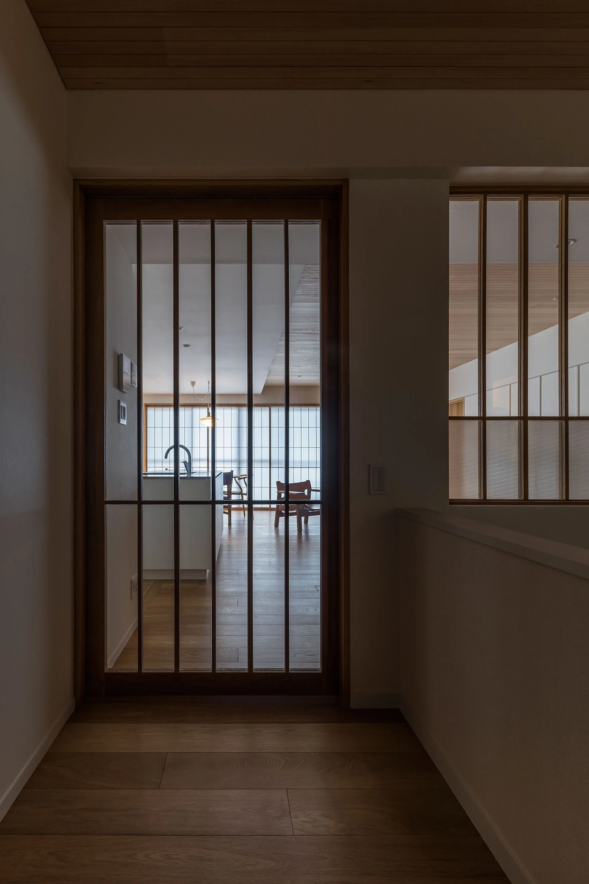A view through a dark wood-framed glass grid door looking into a bright kitchen with a white island and wood floors.