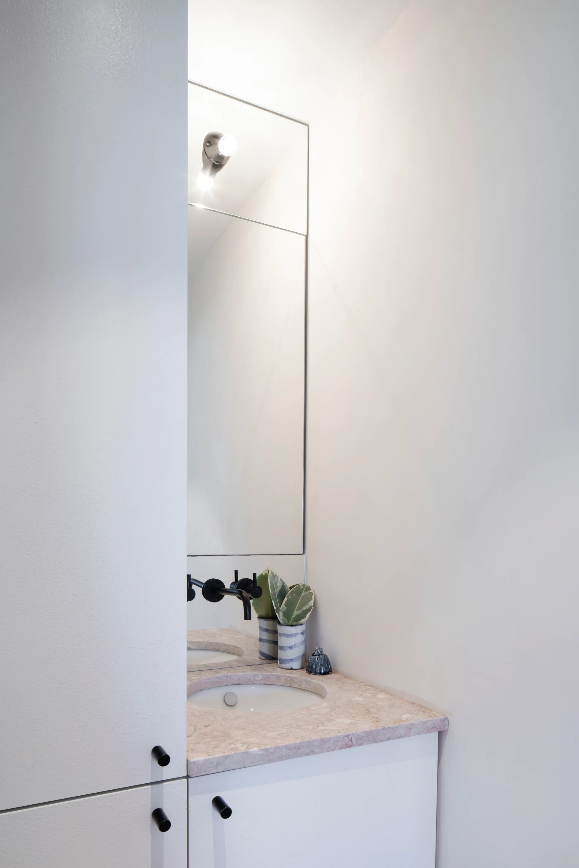 A compact bathroom vanity features a pink marble countertop with an integrated white sink, a wall-mounted matte black faucet, and white cabinets.