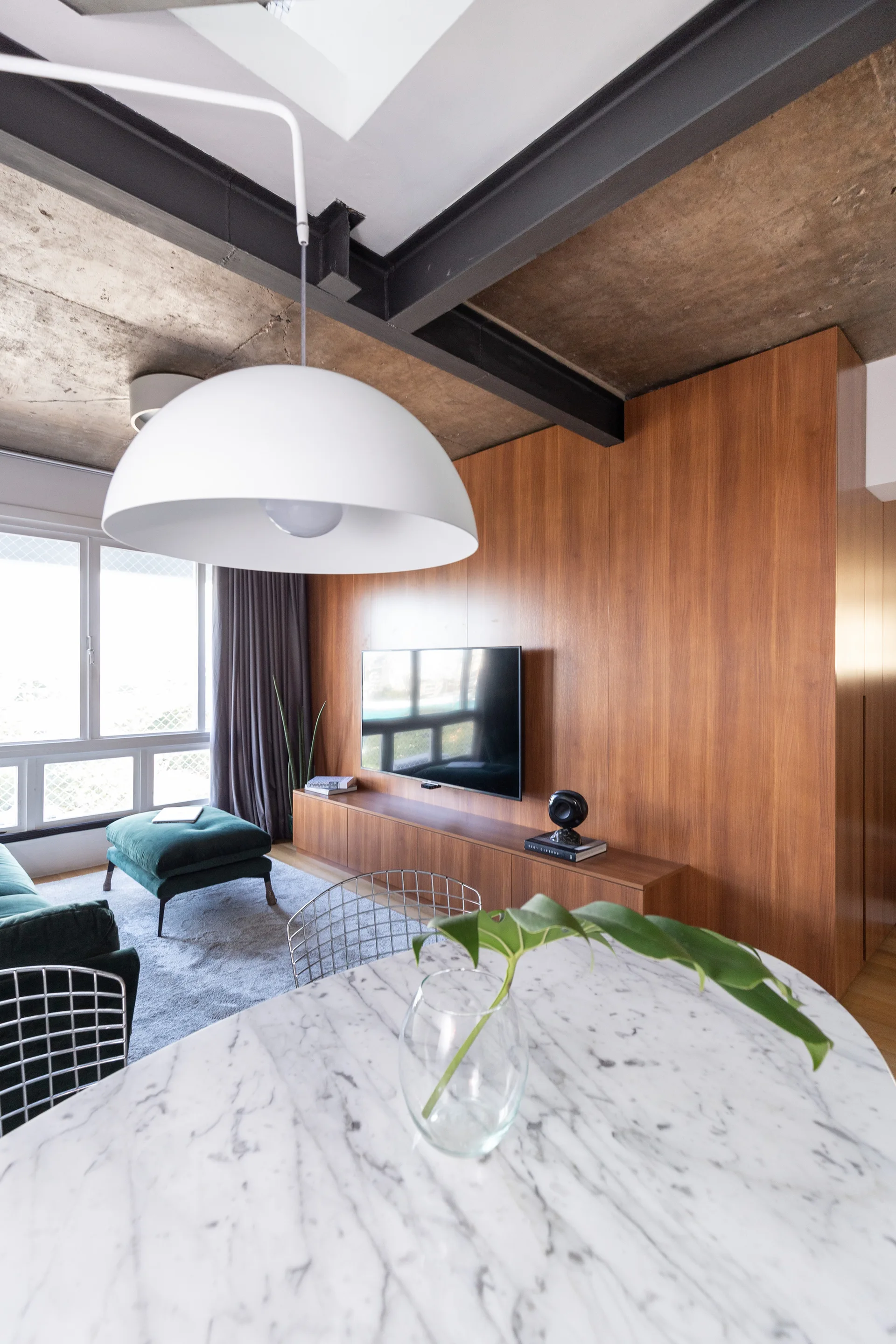 A modern living space featuring a warm wood-paneled wall, an industrial concrete ceiling with steel beams, and a marble-topped dining table.