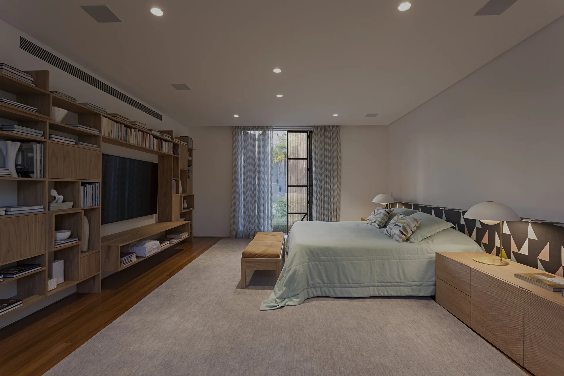 A modern bedroom features a light green bed with a patterned geometric headboard, flanked by wooden nightstands and a large custom wood media wall.