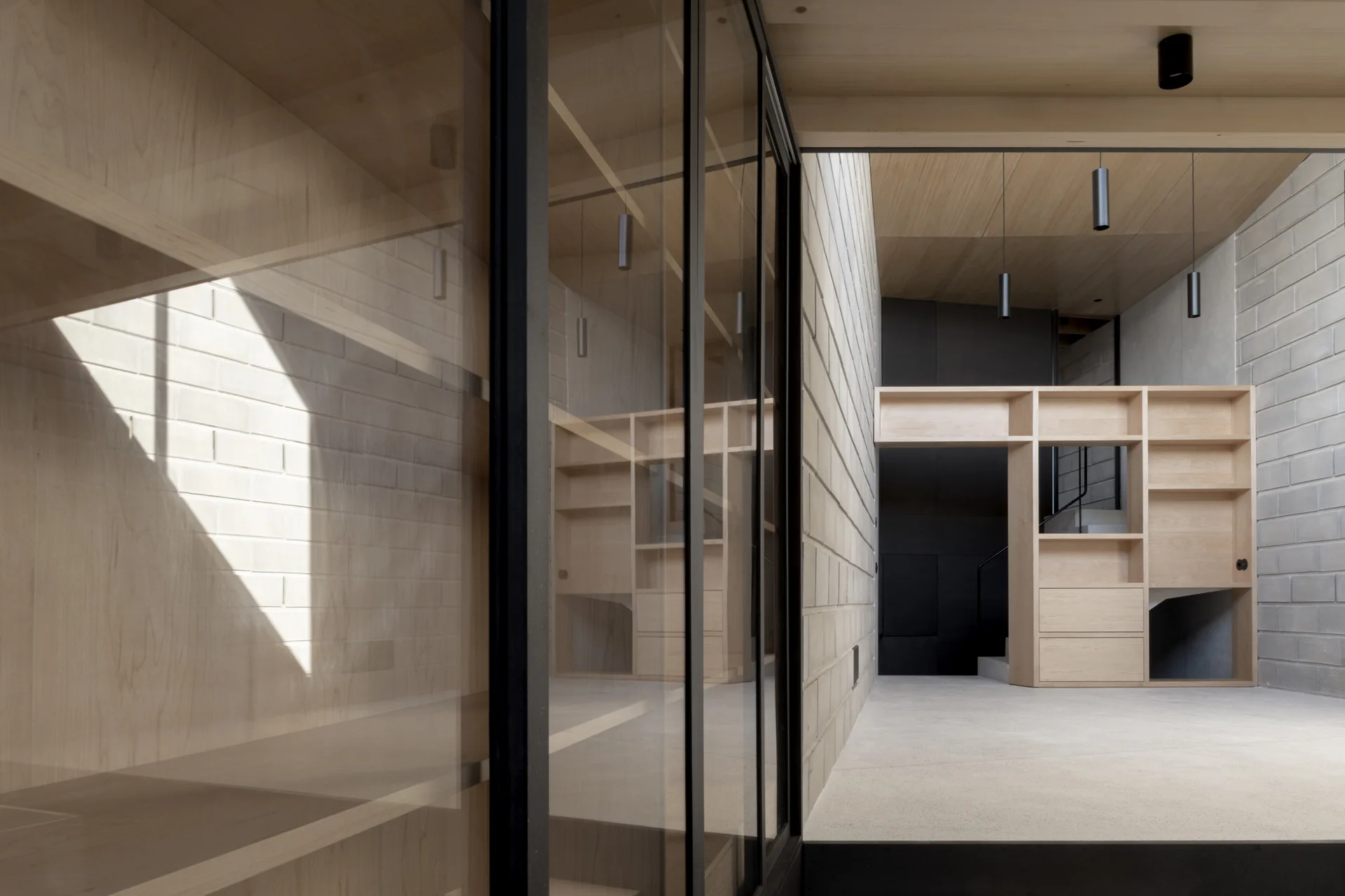 A minimalist hallway features exposed concrete block walls, a light wood paneled ceiling, and custom built-in wooden shelving units.