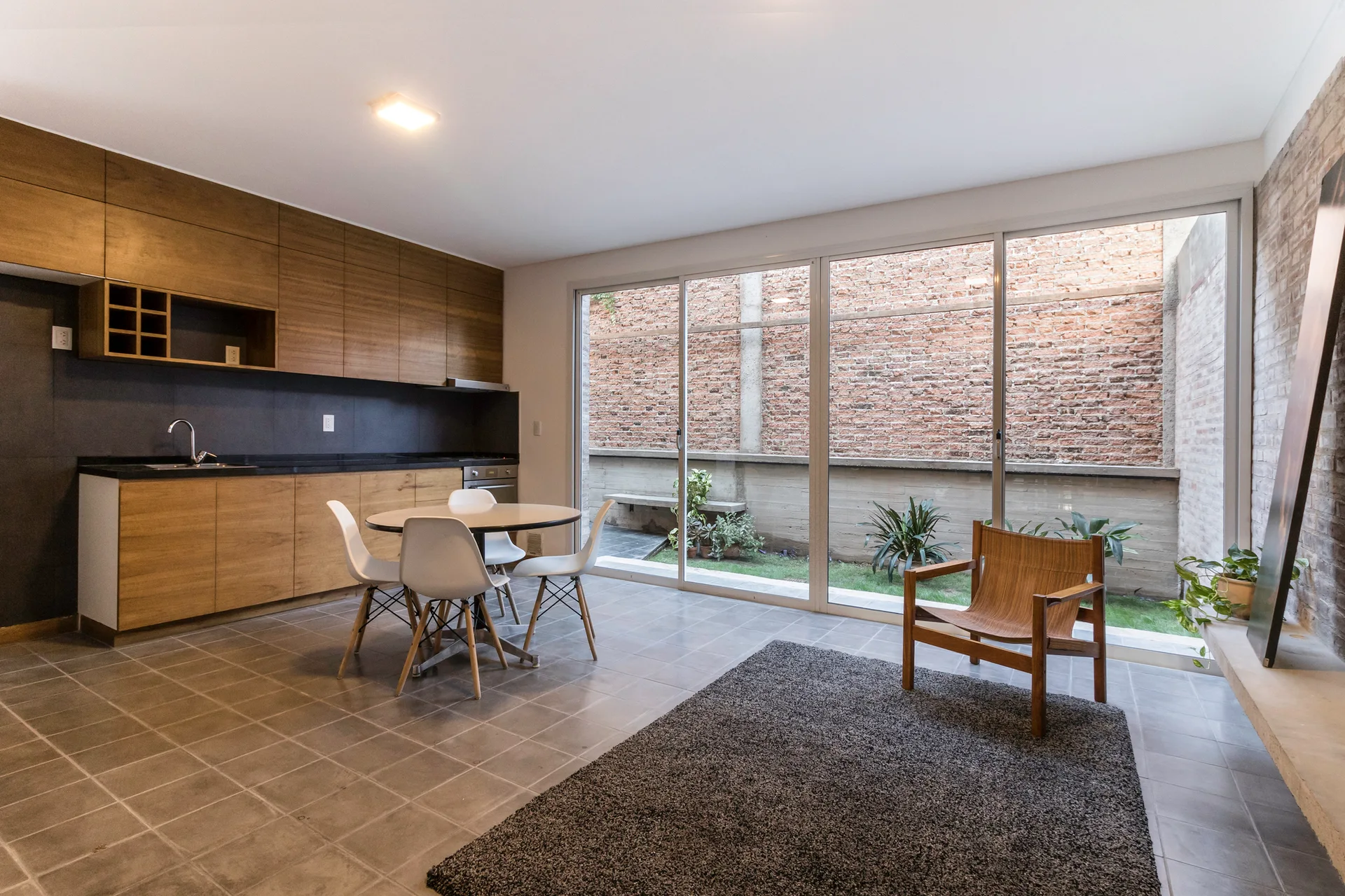 An open kitchen with wood cabinets and a round dining set features large sliding glass doors opening to a brick-walled patio.