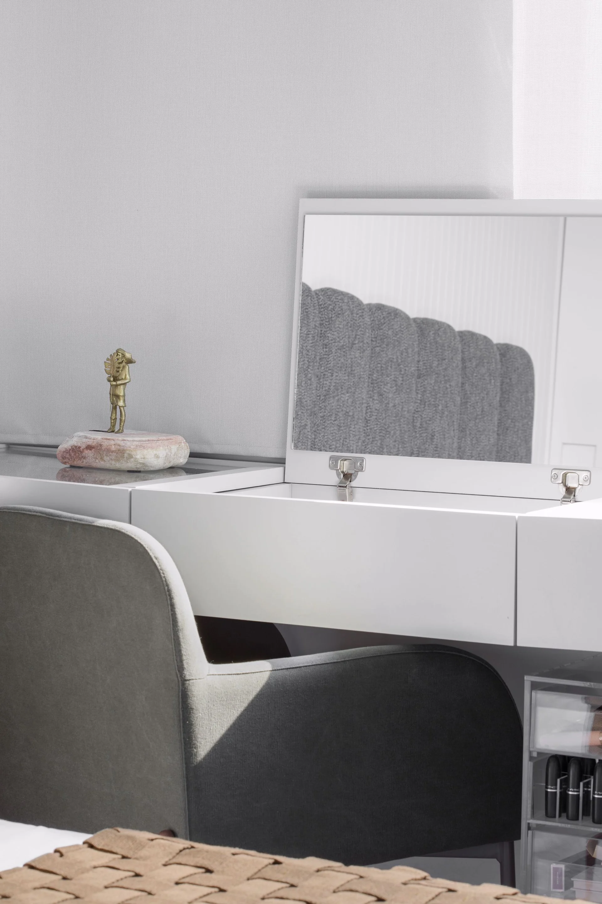 A white vanity table features a hinged lift-up mirror, a grey upholstered chair, and a small decorative figurine.