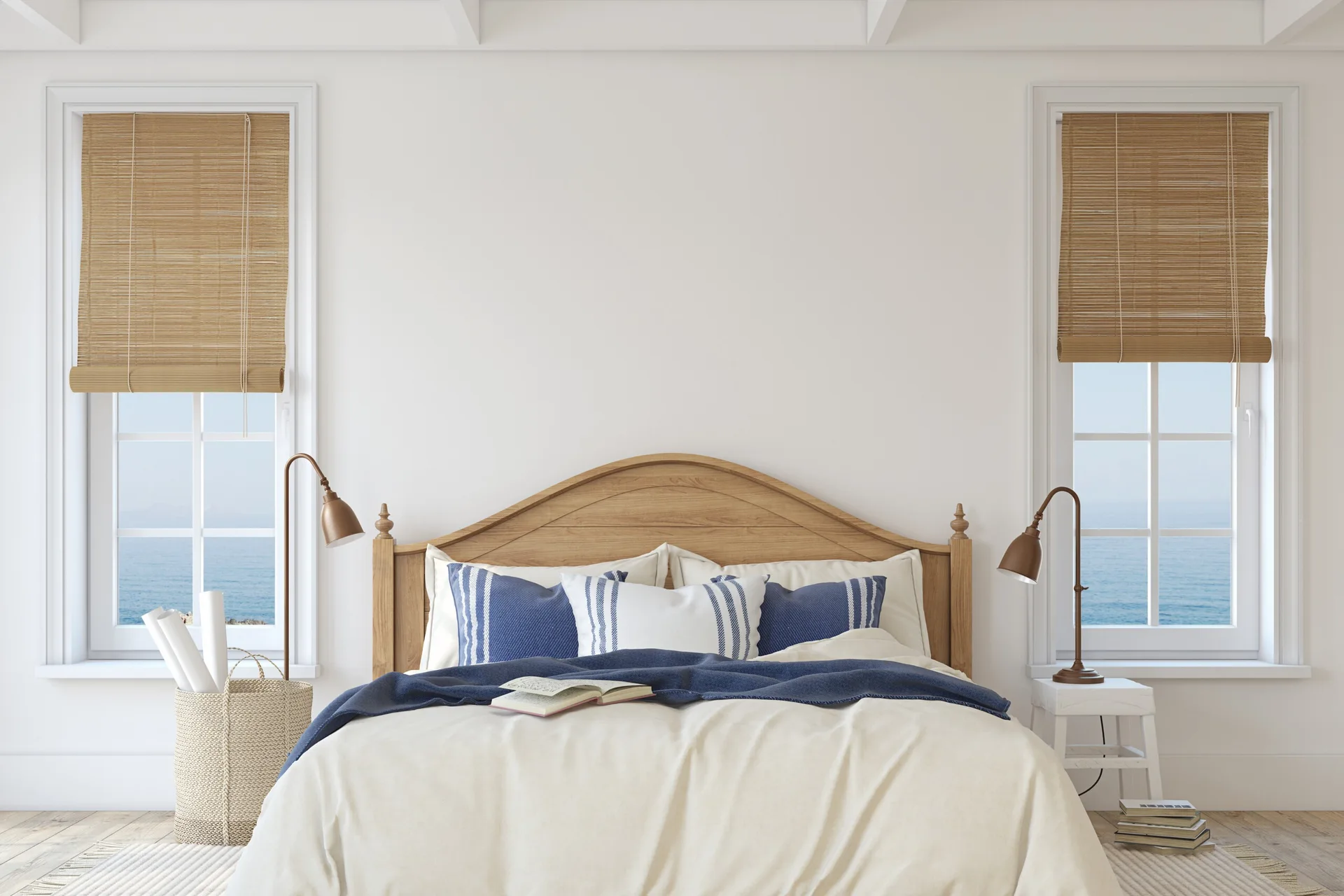 A symmetrical bedroom features a wooden headboard, blue and white striped bedding, and two windows with bamboo blinds overlooking the ocean.