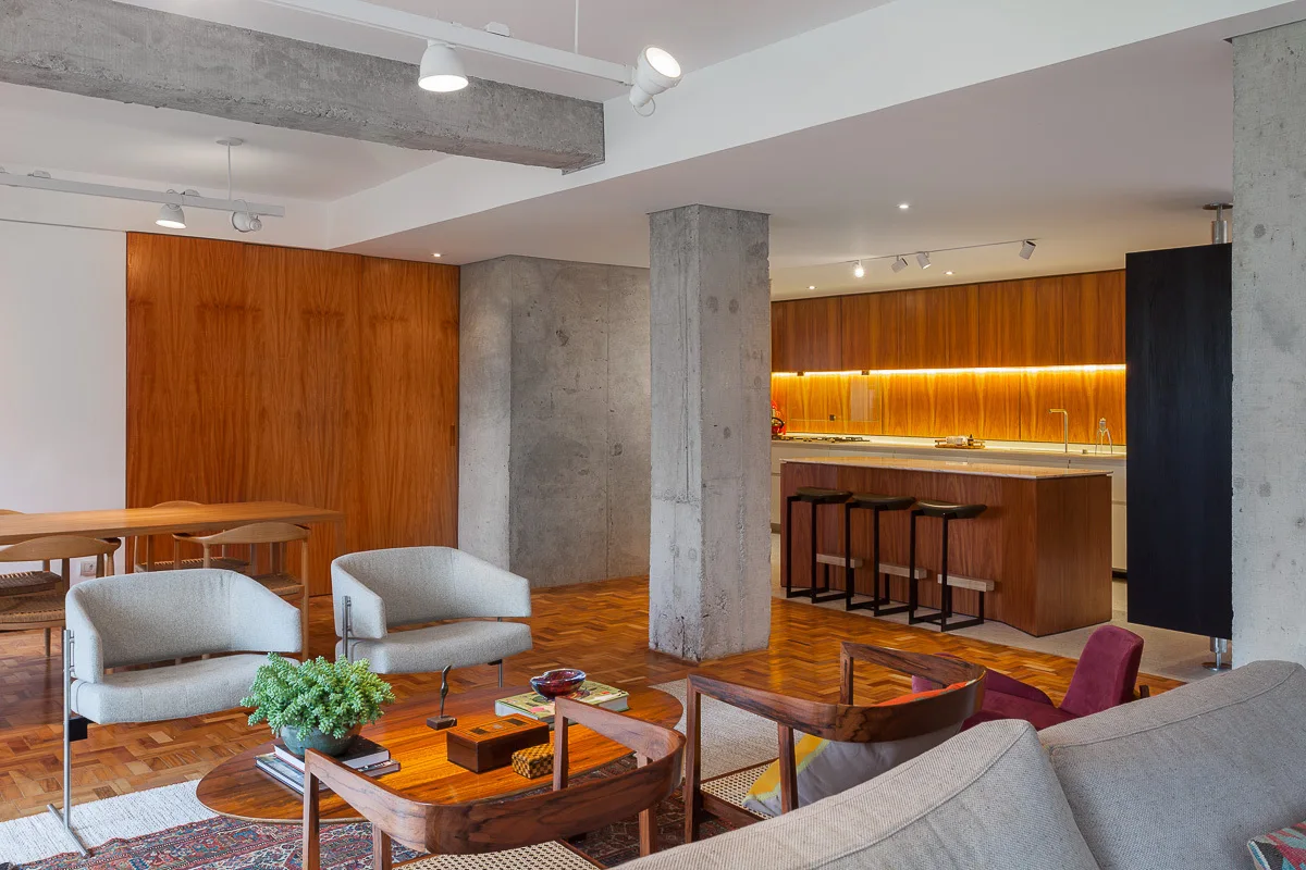 A modern open-concept living space features an exposed concrete column, warm wood-paneled walls, parquet flooring, and mid-century modern furniture.