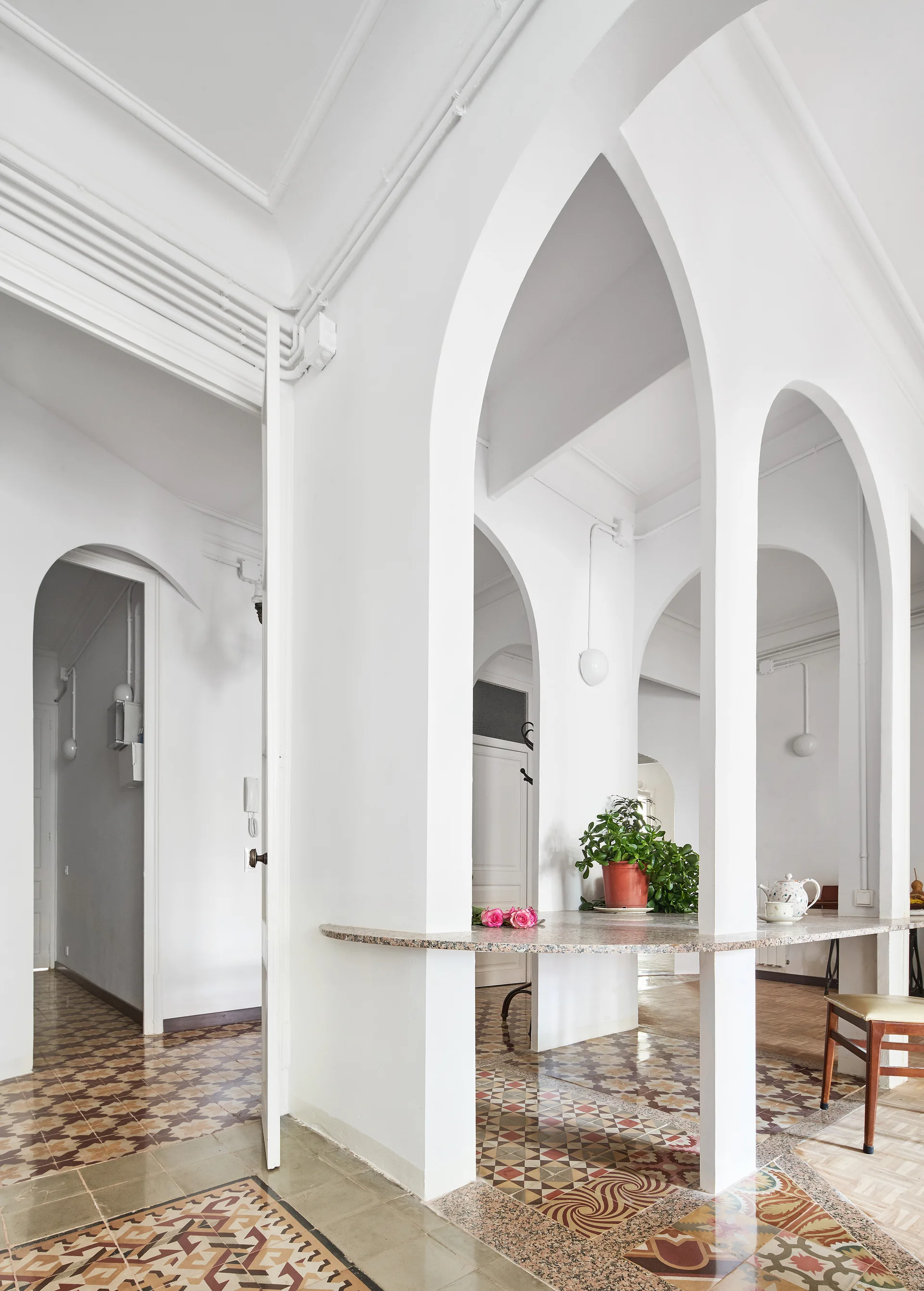 White interior hallway featuring pointed Gothic archways, a built-in stone console table, and patterned geometric floor tiles.