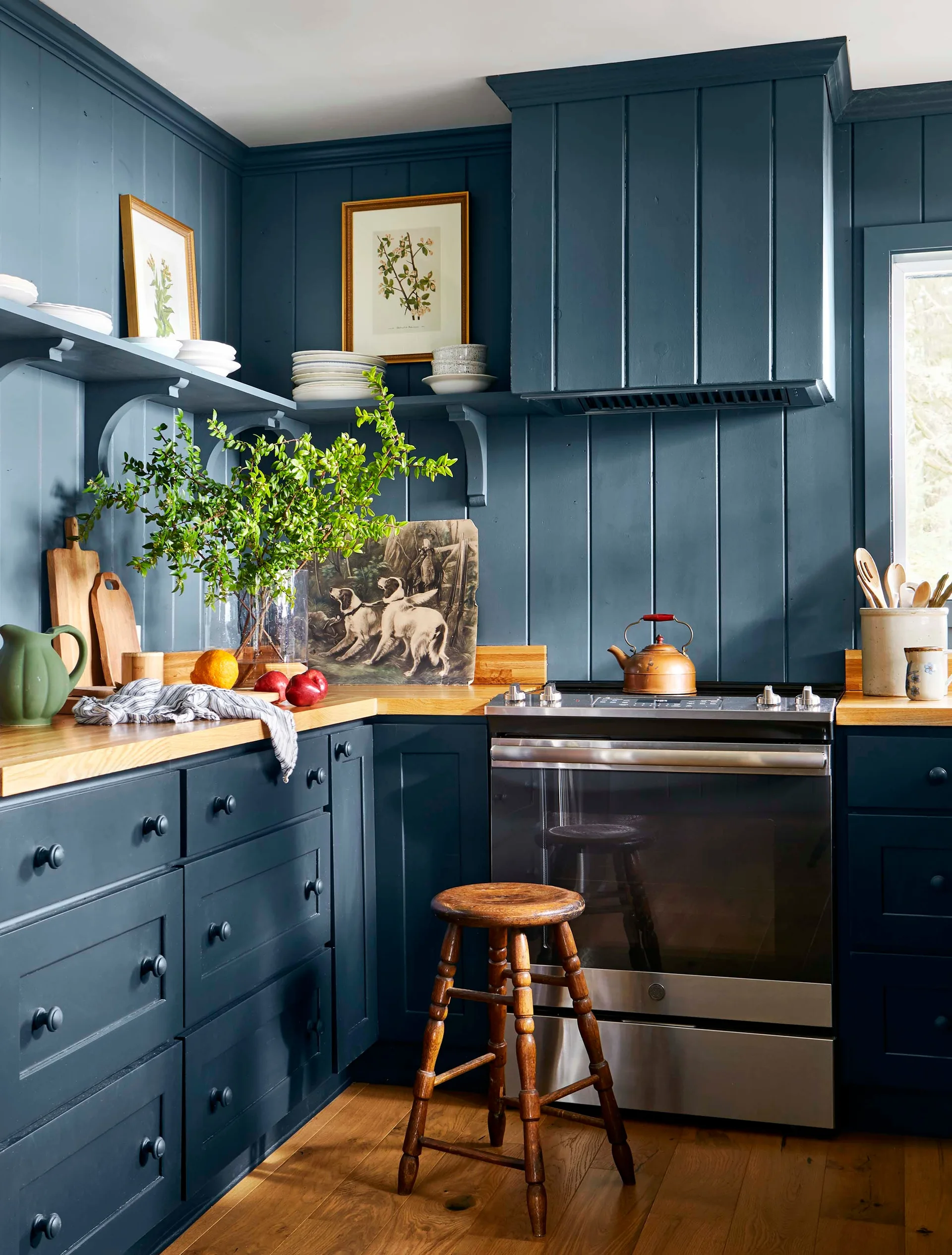 A kitchen with blue vertical wood-paneled walls and matching cabinets with warm wood countertops next to a stainless steel stove.