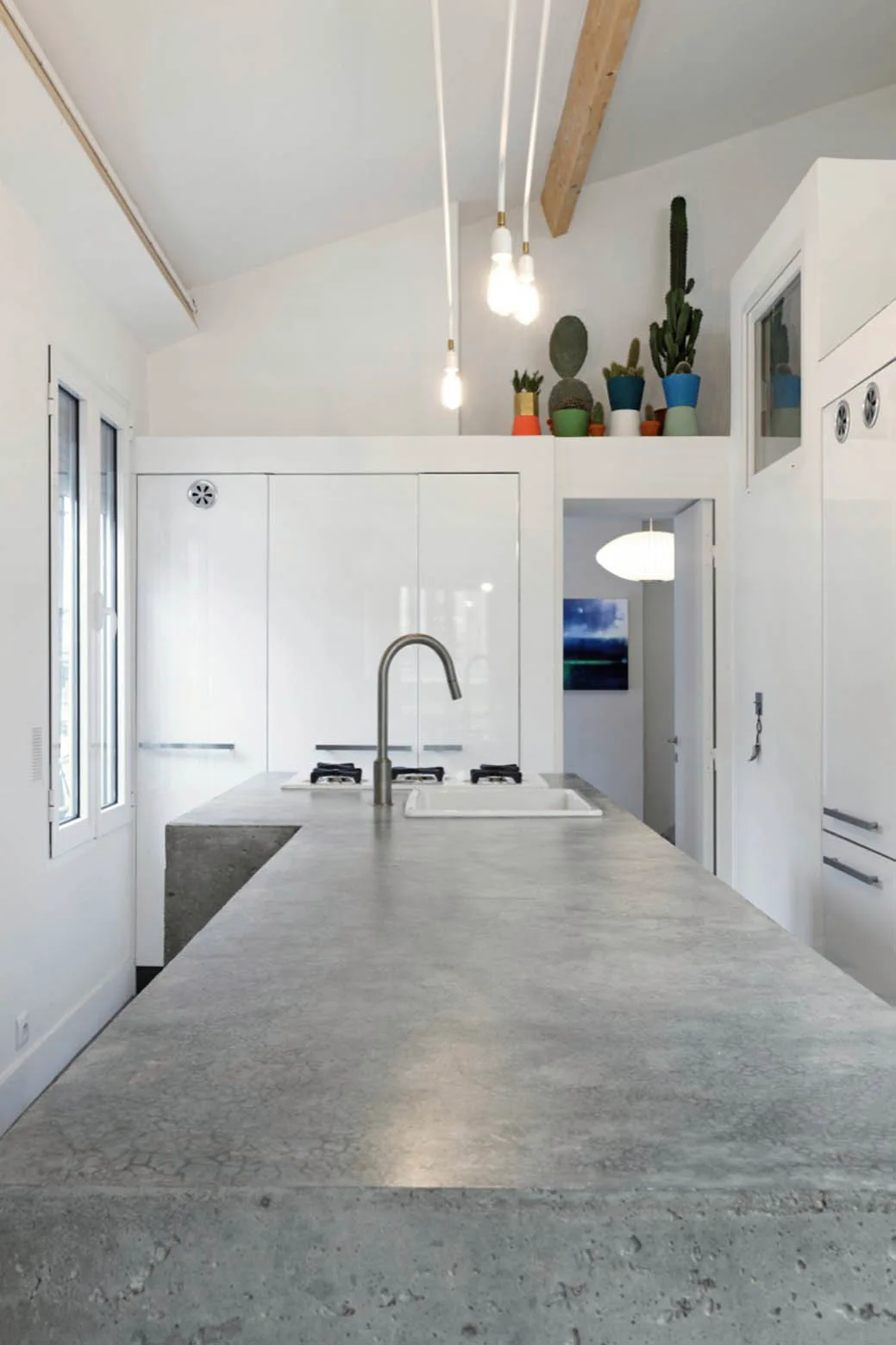 A minimalist kitchen showcases a textured grey concrete island with an integrated sink alongside sleek glossy white cabinets.