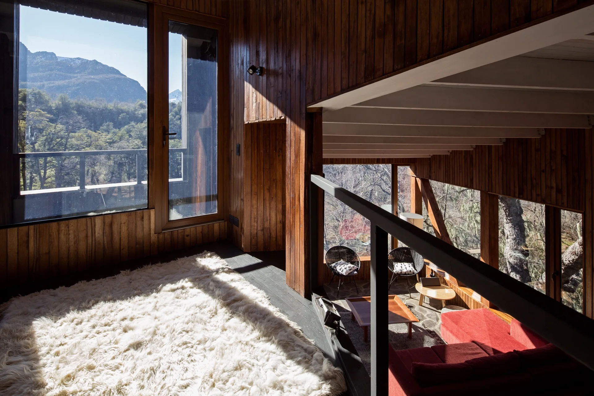 A split-level cabin interior featuring a raised platform with a white shag rug next to a lower living area with a red sofa and wood paneled walls.