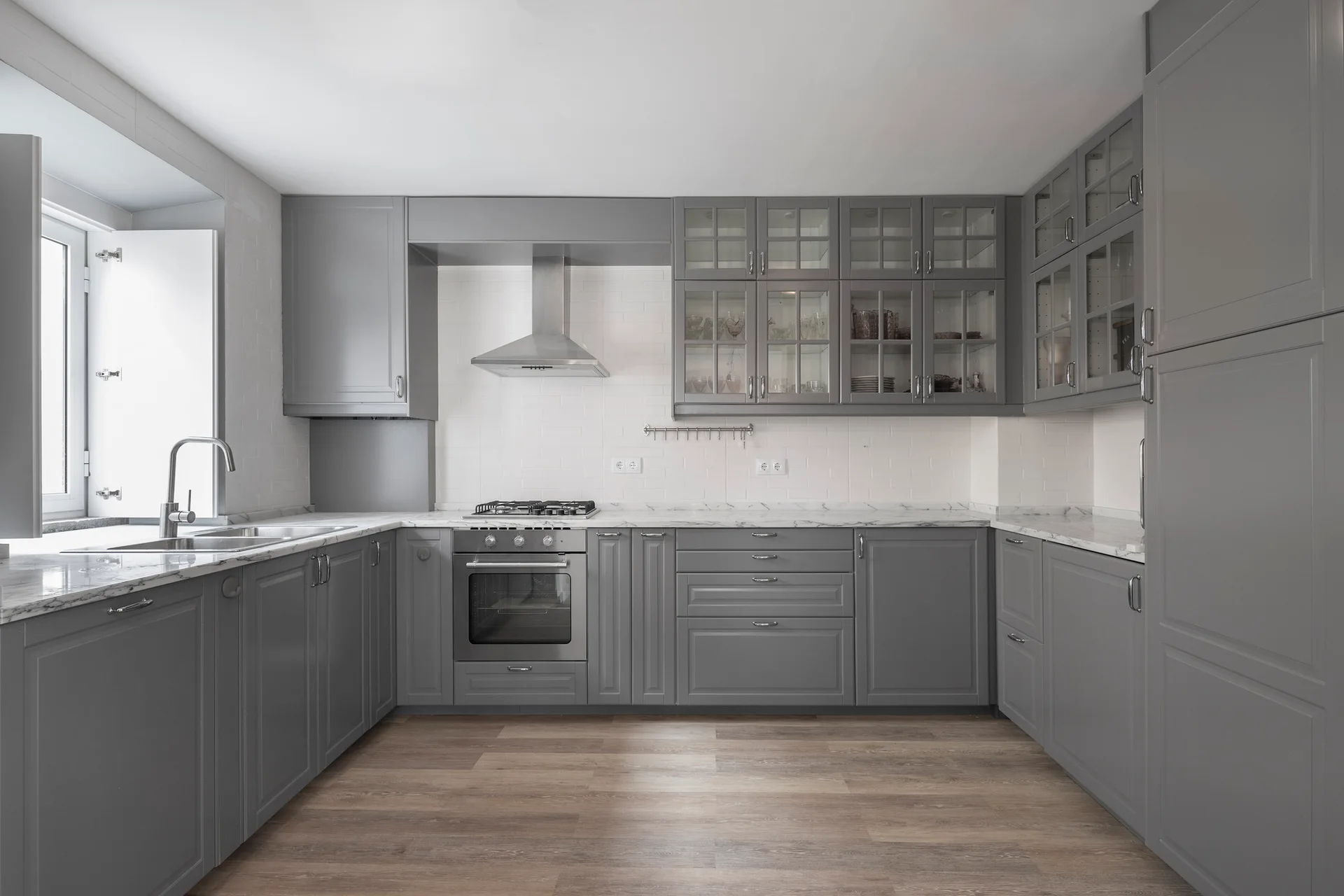 A U-shaped kitchen featuring grey shaker cabinets, white marble-patterned countertops, a tiled backsplash, and wood-look flooring.
