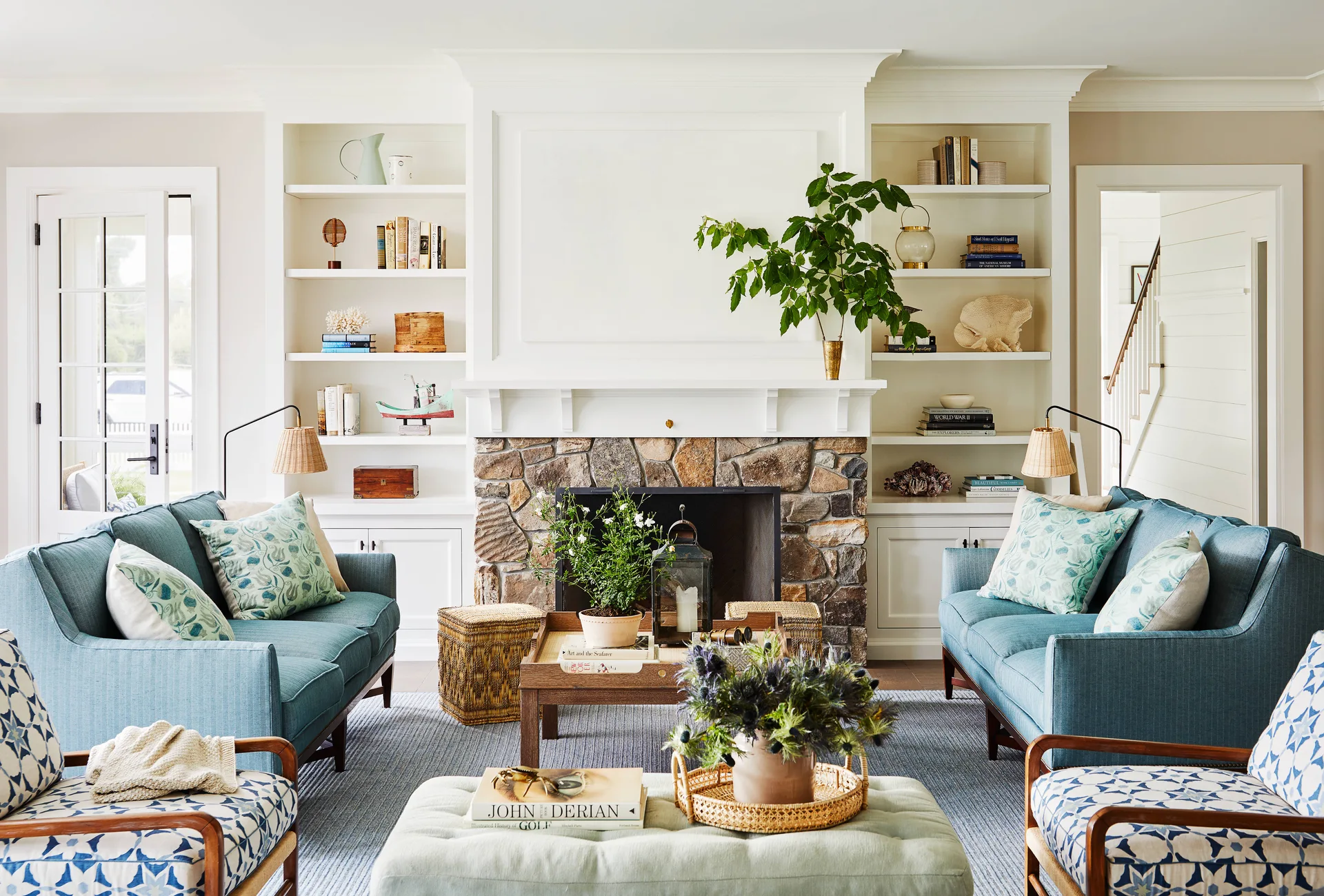 A symmetrical living room features two blue sofas facing each other beside a central stone fireplace with built-in white bookshelves.