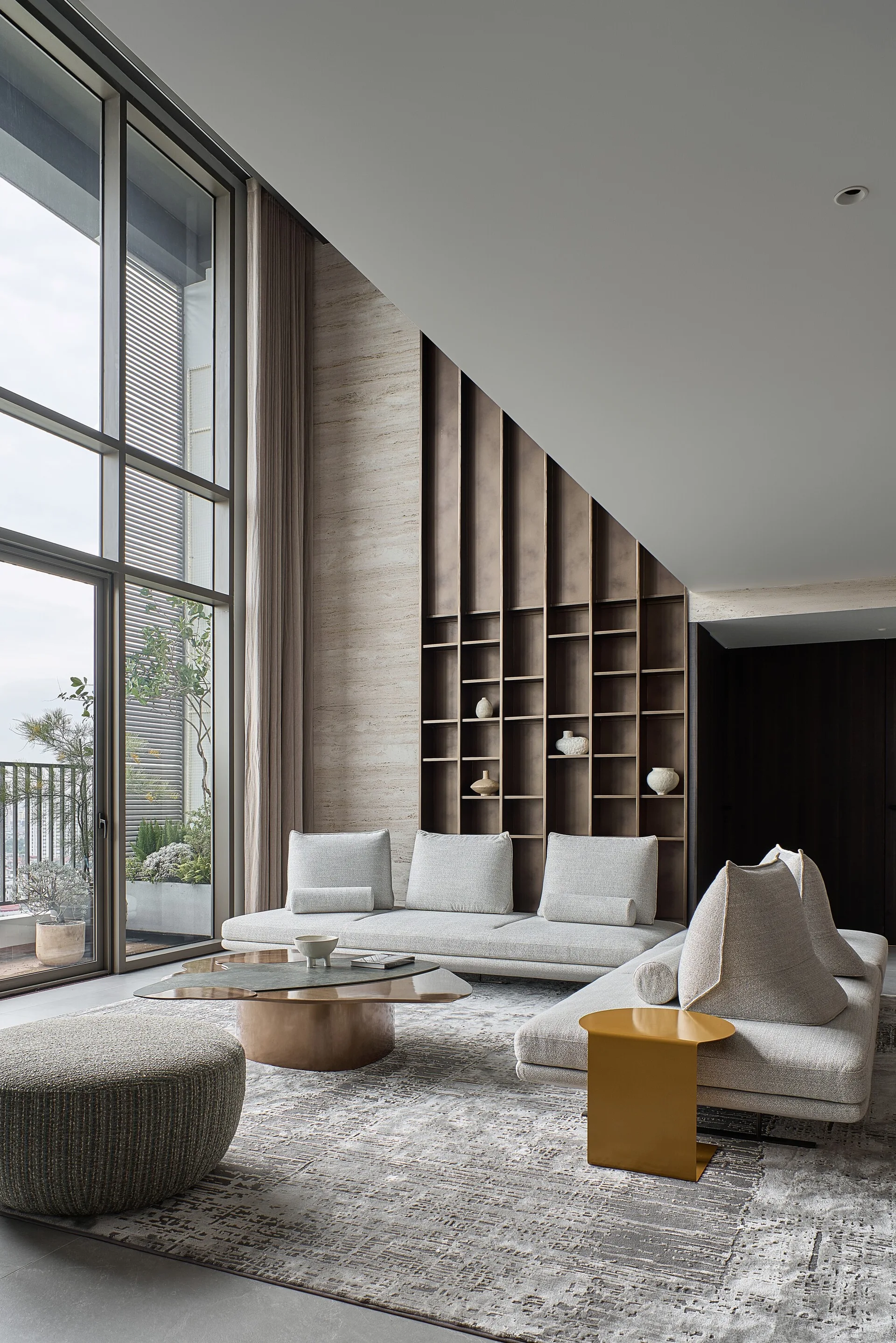 A contemporary living room featuring a low grey modular sofa, an organic bronze coffee table, and a tall built-in metal shelving unit.