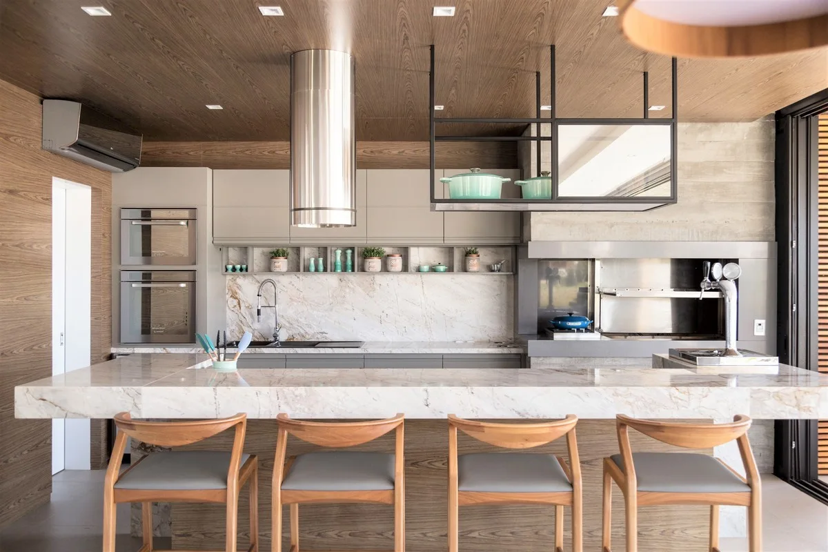 A modern kitchen with a marble waterfall island, wooden barstools, a wood-paneled ceiling, and integrated grey cabinets.