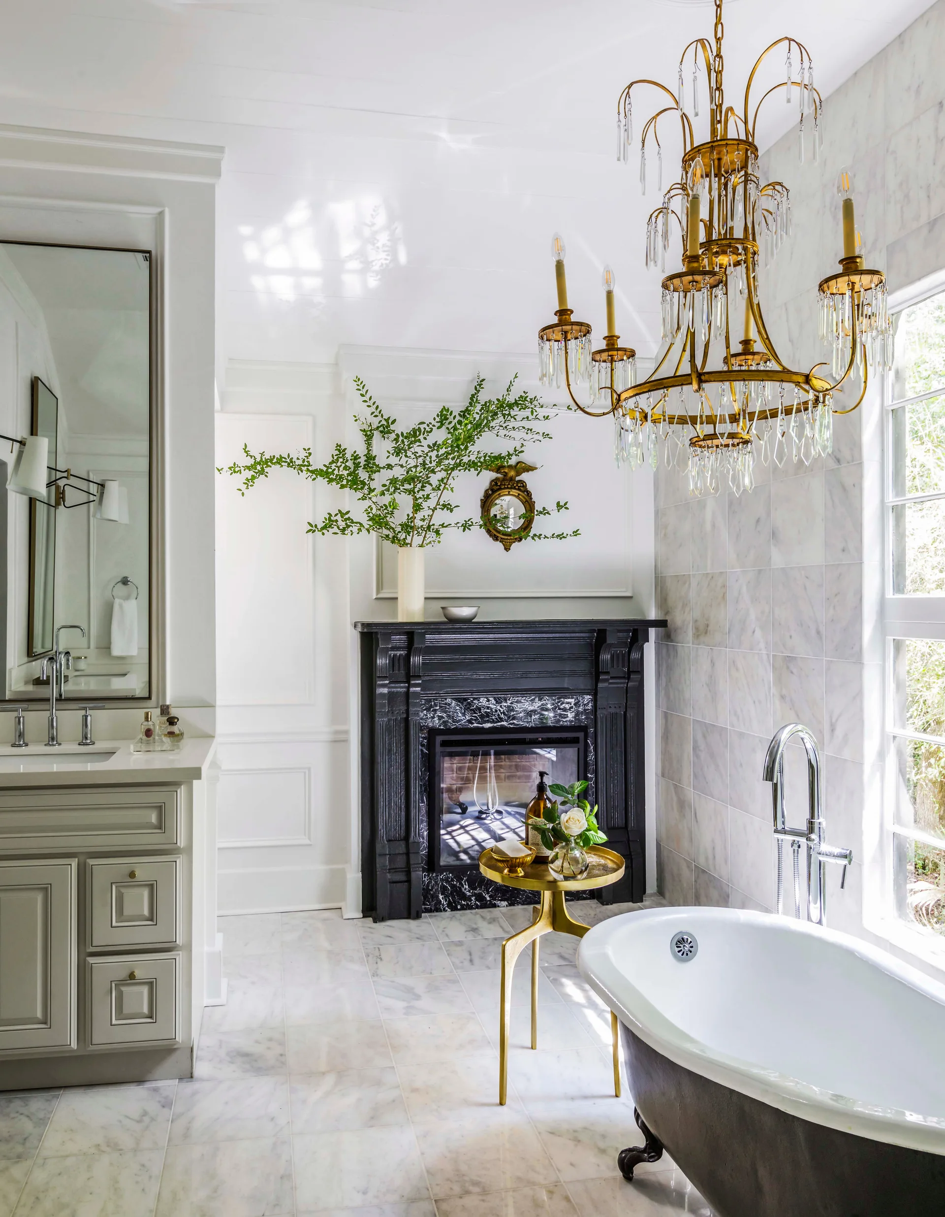 A bathroom featuring a freestanding clawfoot tub, a black fireplace with a marble surround, and an ornate gold chandelier hanging from the ceiling.