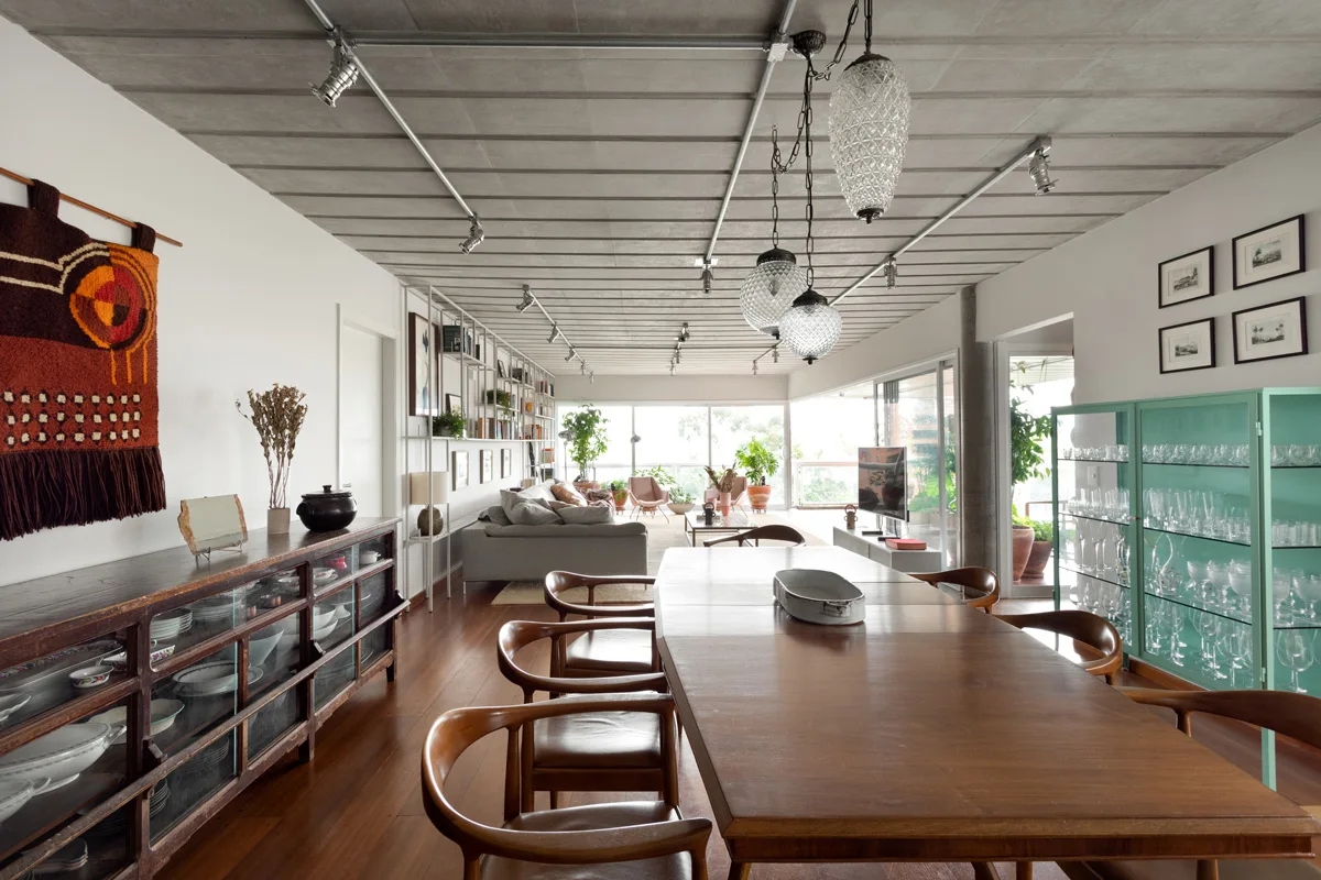 An open-plan dining room features a wooden table and chairs beneath a concrete ceiling, beside a mint green display cabinet.