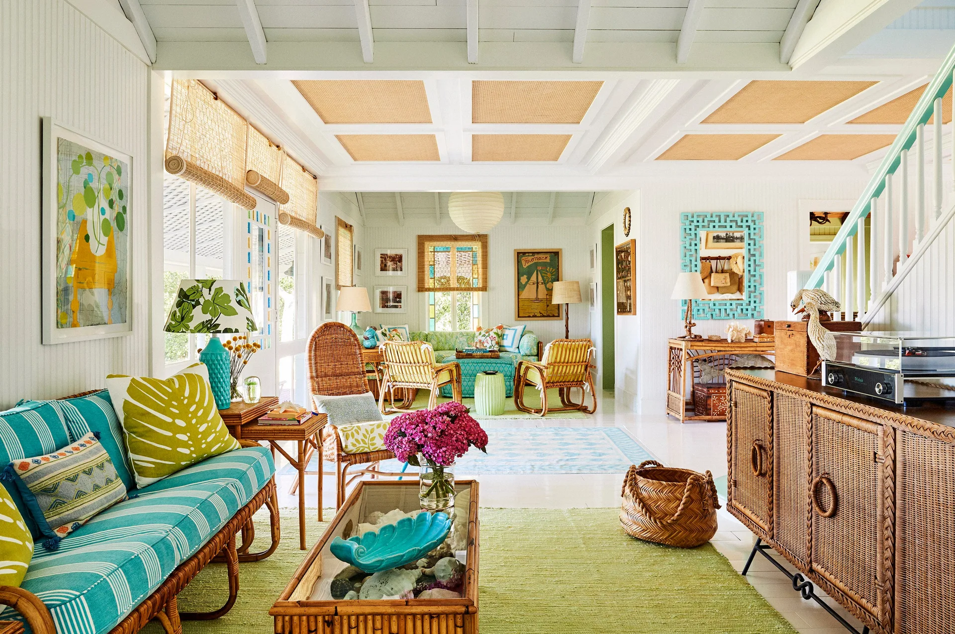 Bright coastal living room with white paneled walls, a turquoise striped sofa, rattan armchairs, and coffered ceiling with woven inserts.