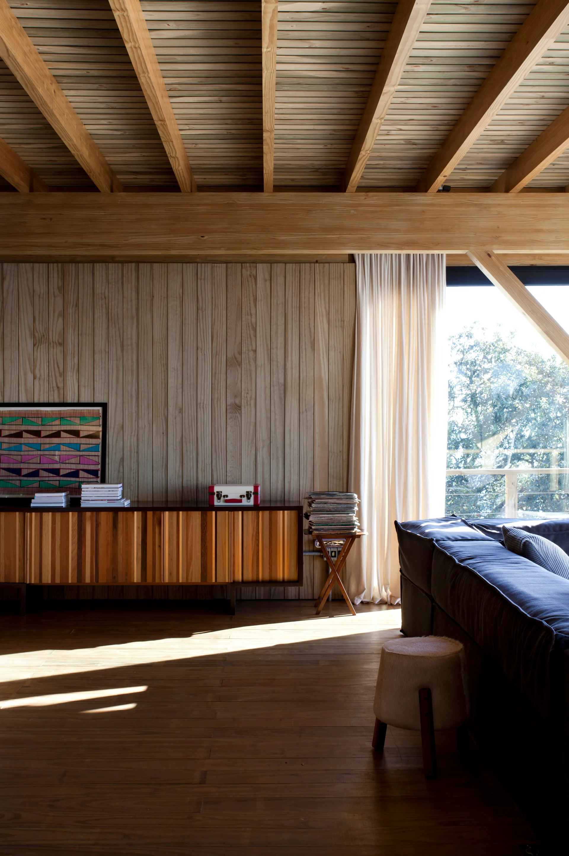 A rustic living room features a wooden credenza against vertical plank walls under an exposed timber ceiling next to a dark sofa.