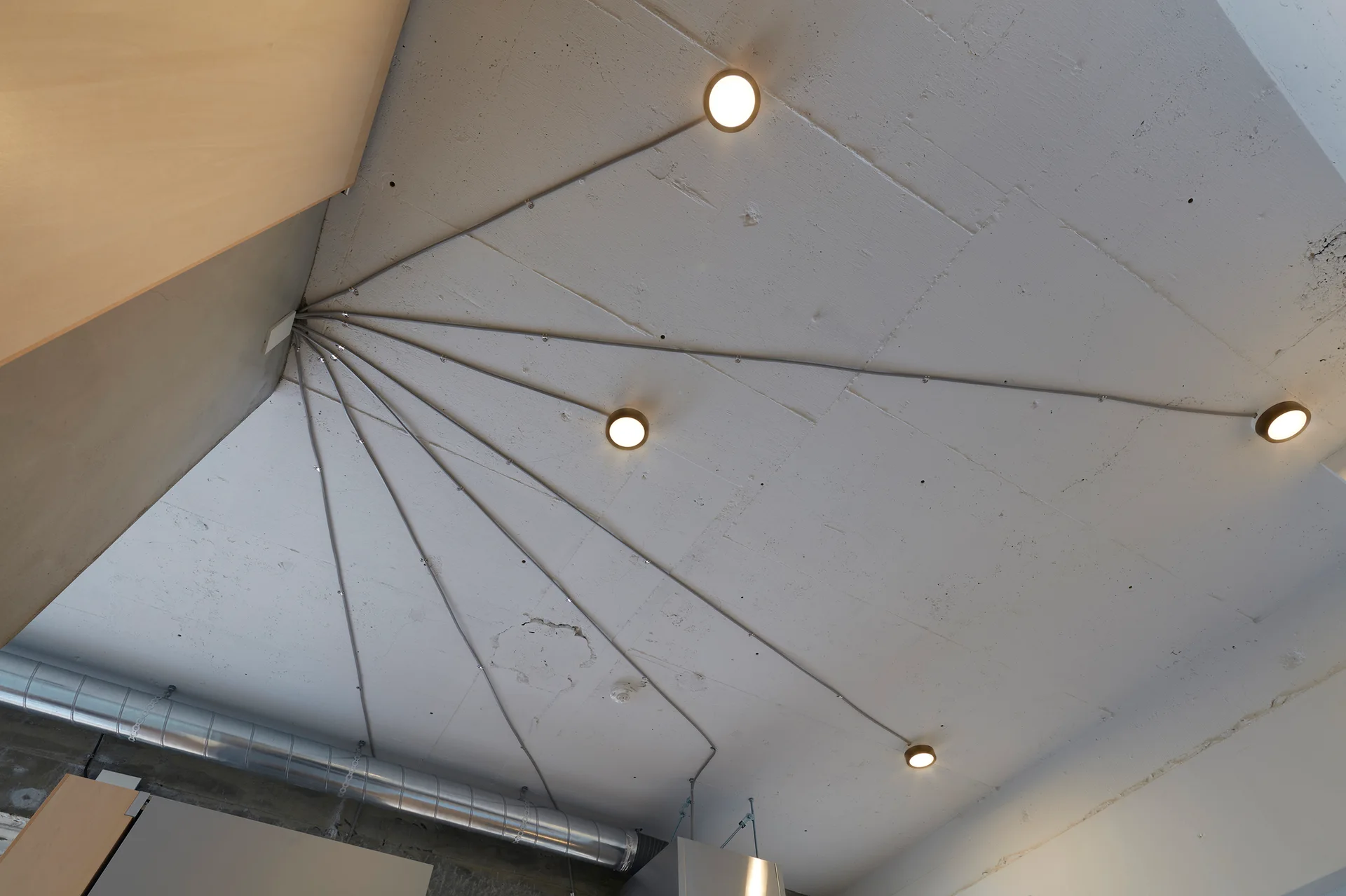 Surface-mounted electrical conduits radiate from a corner across a white painted concrete ceiling to circular flush-mount light fixtures.