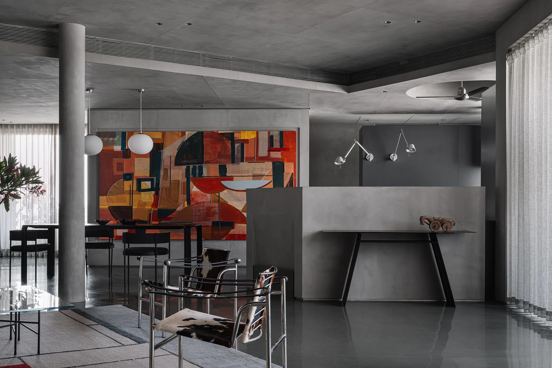 An industrial open-plan living and dining space features raw concrete walls, cowhide sling chairs, and a large abstract painting in orange and red.