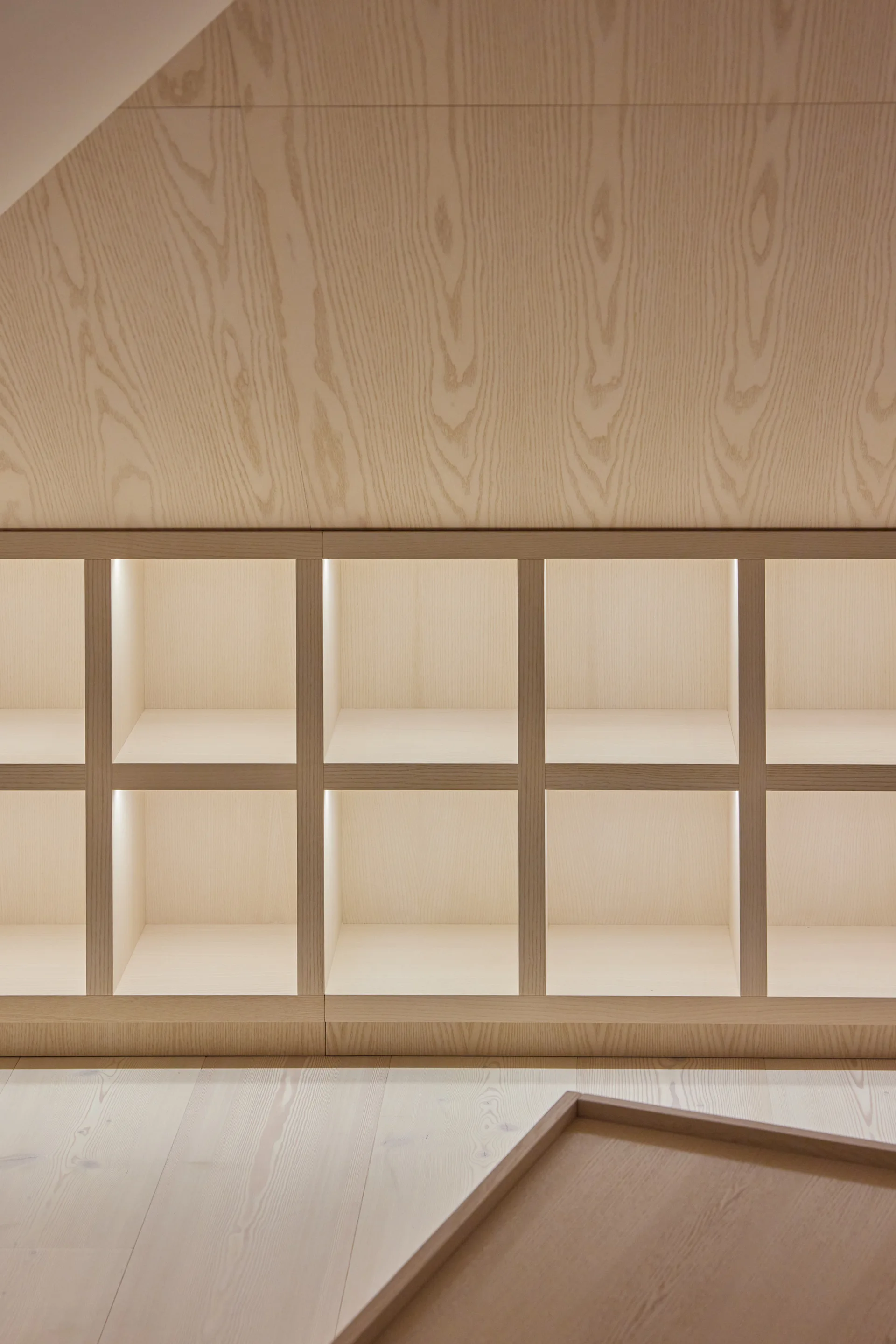 A custom light wood grid shelving unit built under an angled wood-paneled wall features integrated vertical LED strip lights in each cubby.