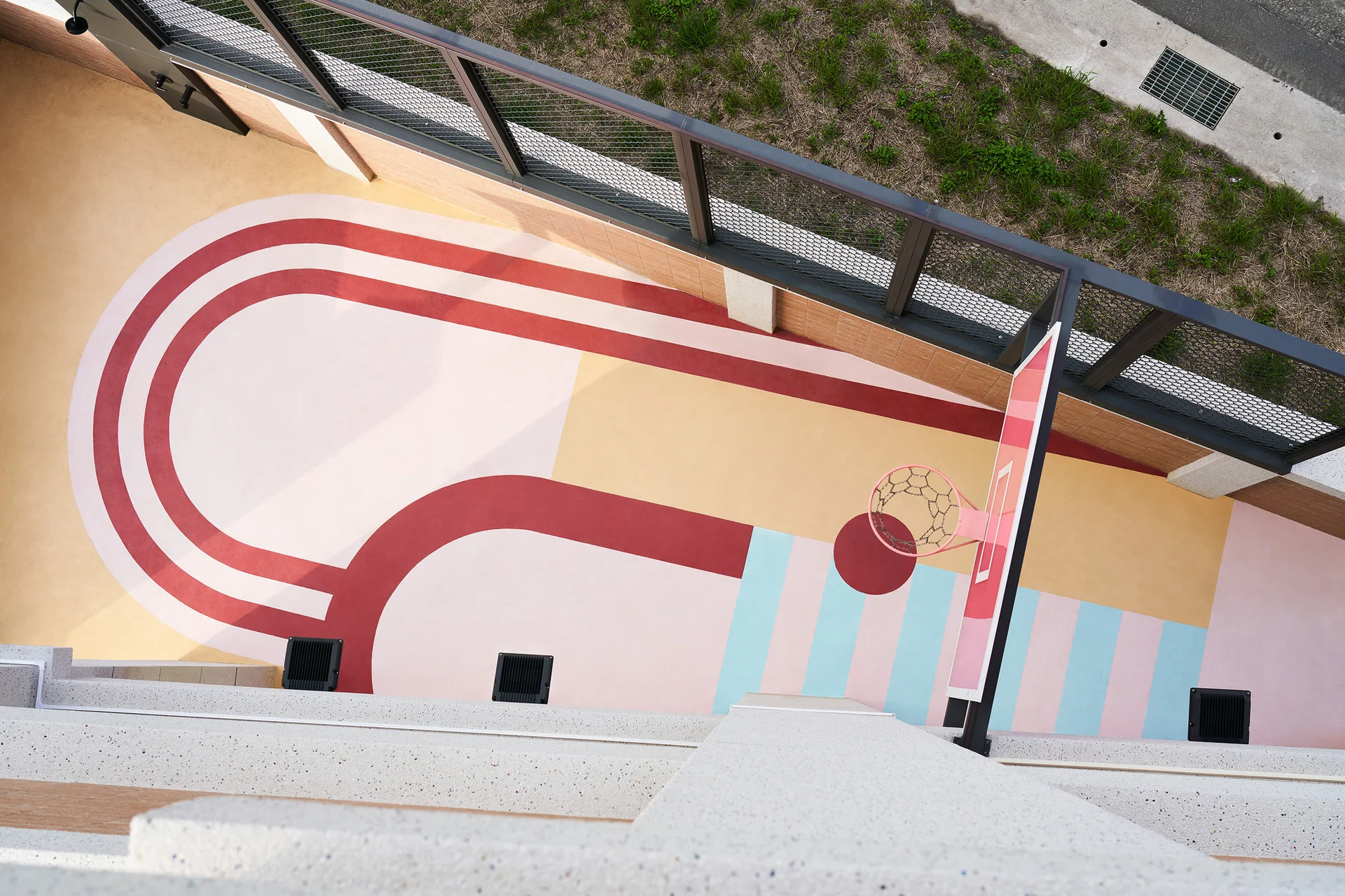 An overhead view of an outdoor sports court with a colorful geometric painted concrete surface and a pink basketball hoop.