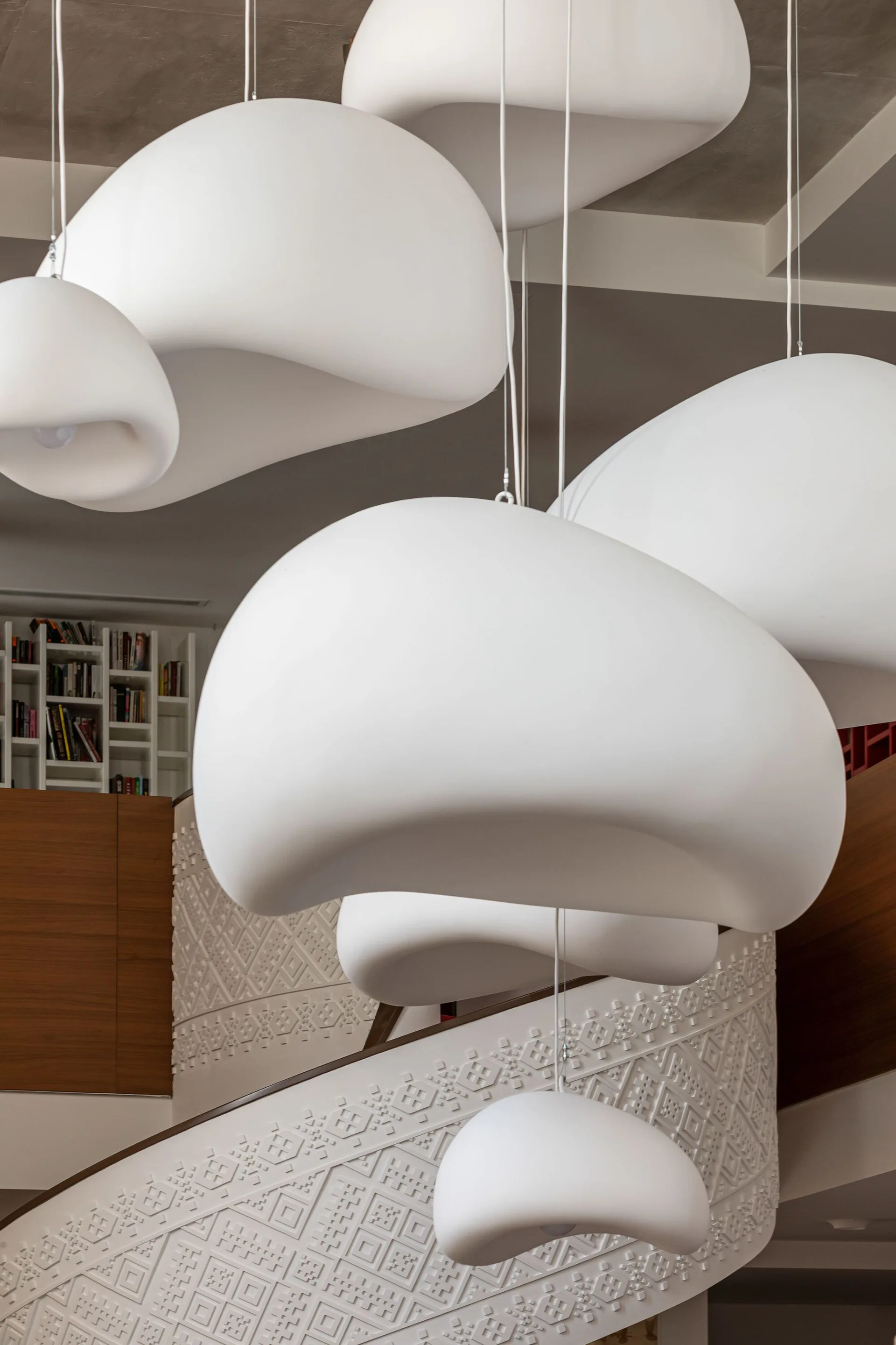 Several large, organic-shaped white pendant lights hang in a cluster above a winding staircase with a textured geometric relief pattern.
