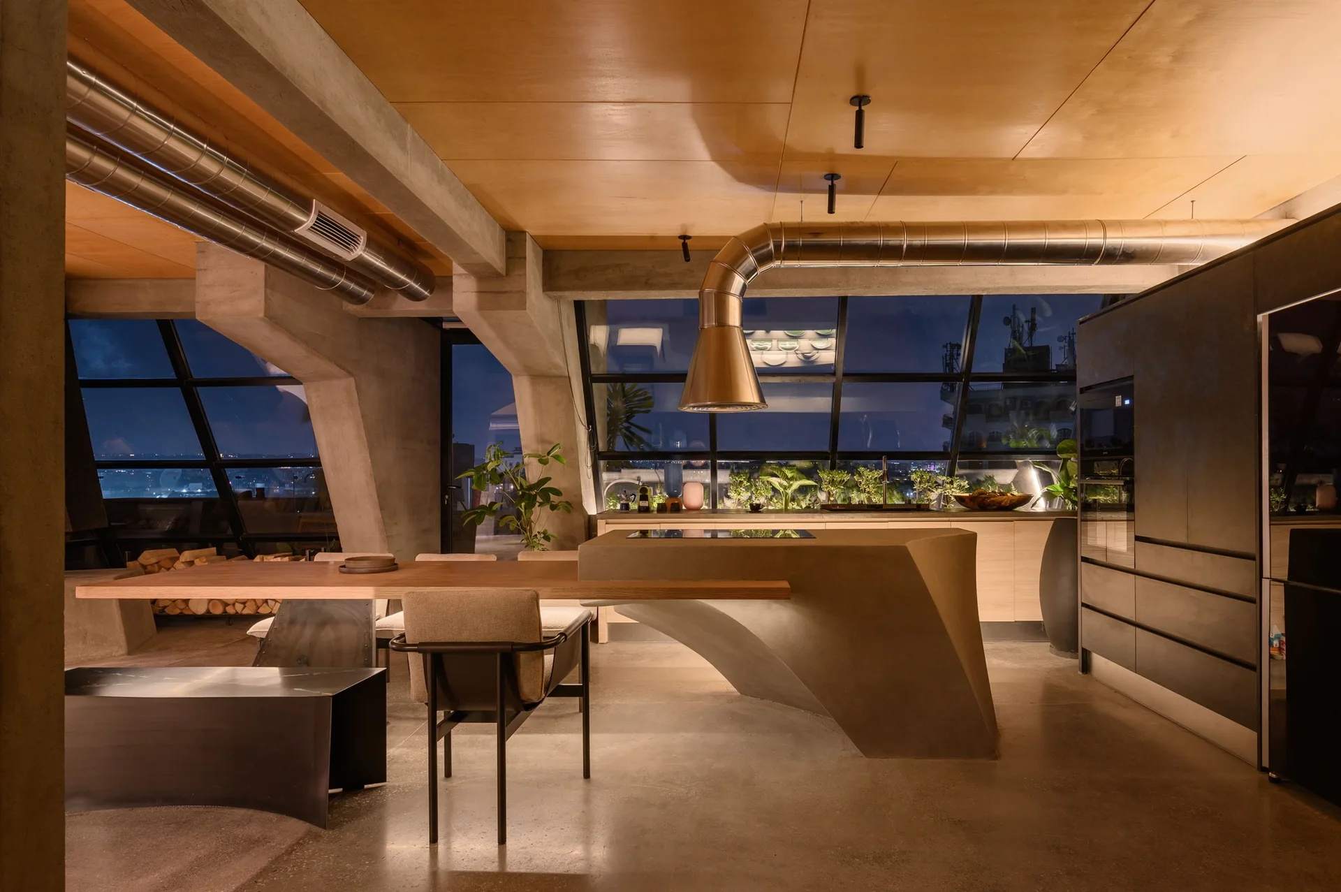 An industrial loft kitchen features a sculptural concrete island connected to a wood dining table under a wood ceiling with exposed metal ductwork.