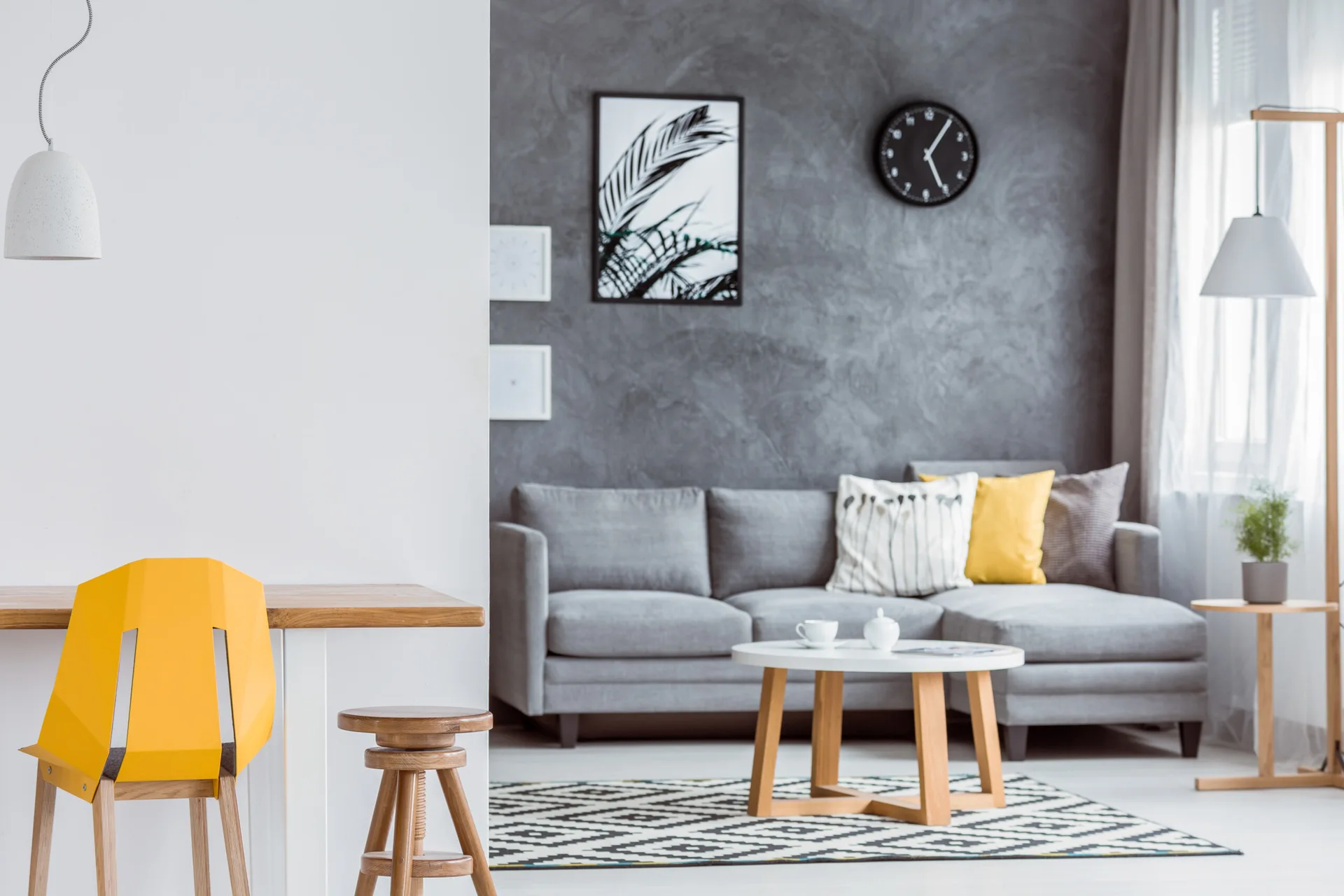 A grey sectional sofa is positioned against a dark textured plaster wall in a living room with a geometric area rug.