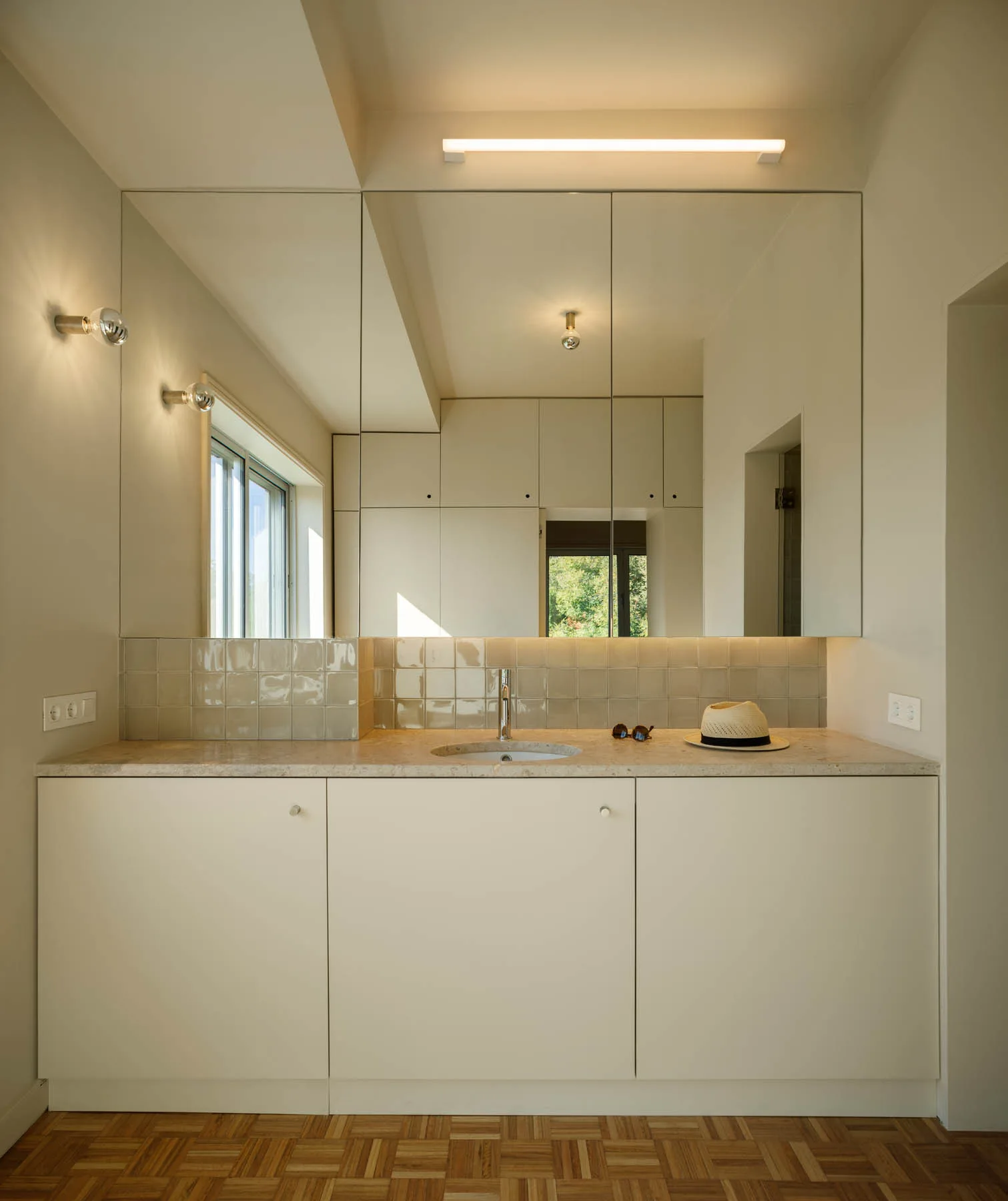 An off-white minimalist bathroom vanity with a square tile backsplash, stone countertop, integrated mirror, and parquet wood flooring.