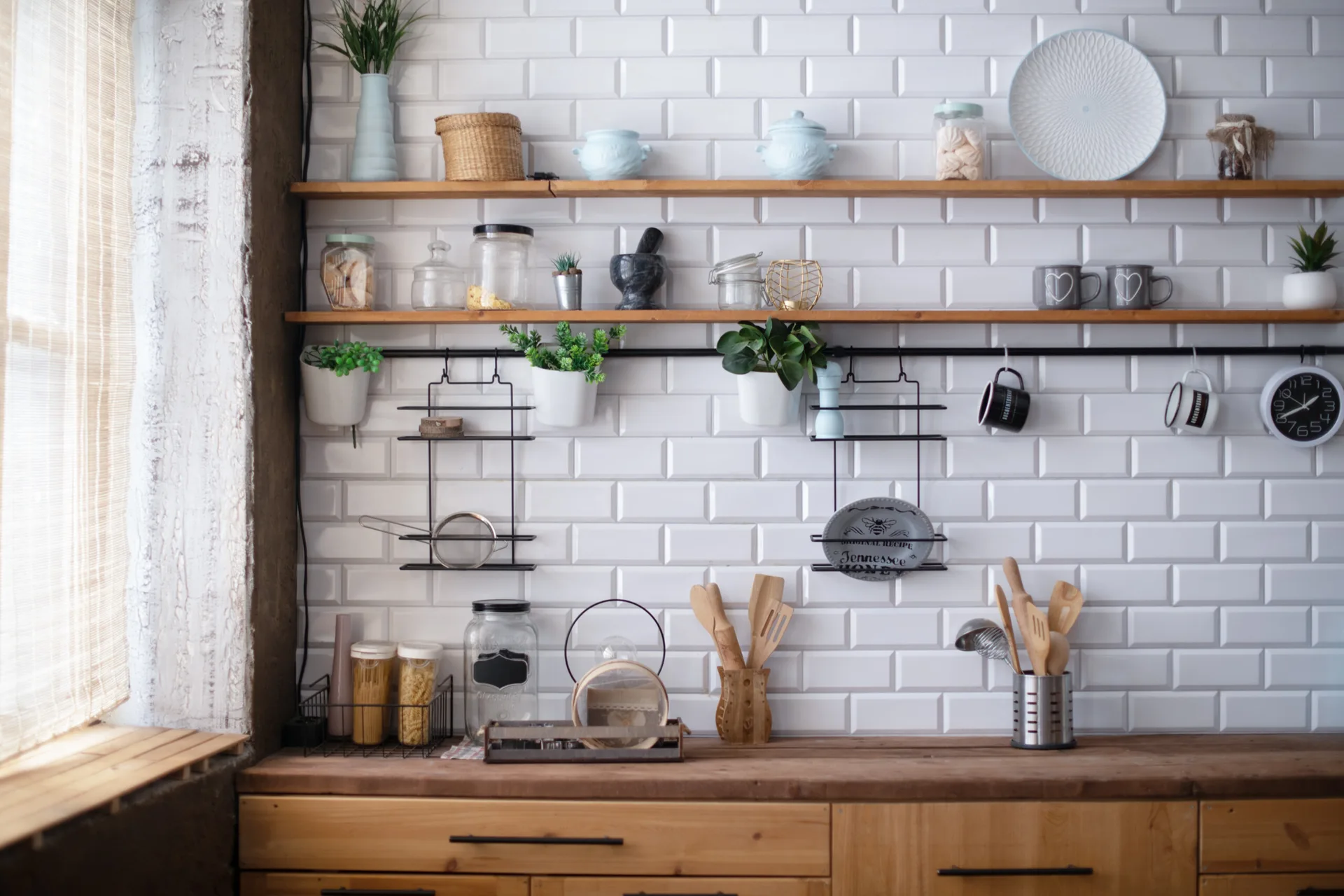 Wooden open shelves and a hanging black metal organizer are mounted on a white subway tile backsplash above a wood countertop.