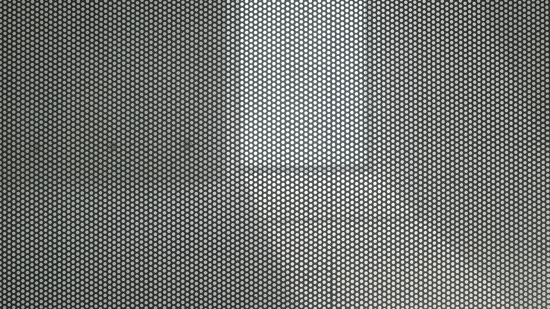 A close-up view of a grey metal sheet featuring a uniform grid of circular perforations highlighted by directional lighting.
