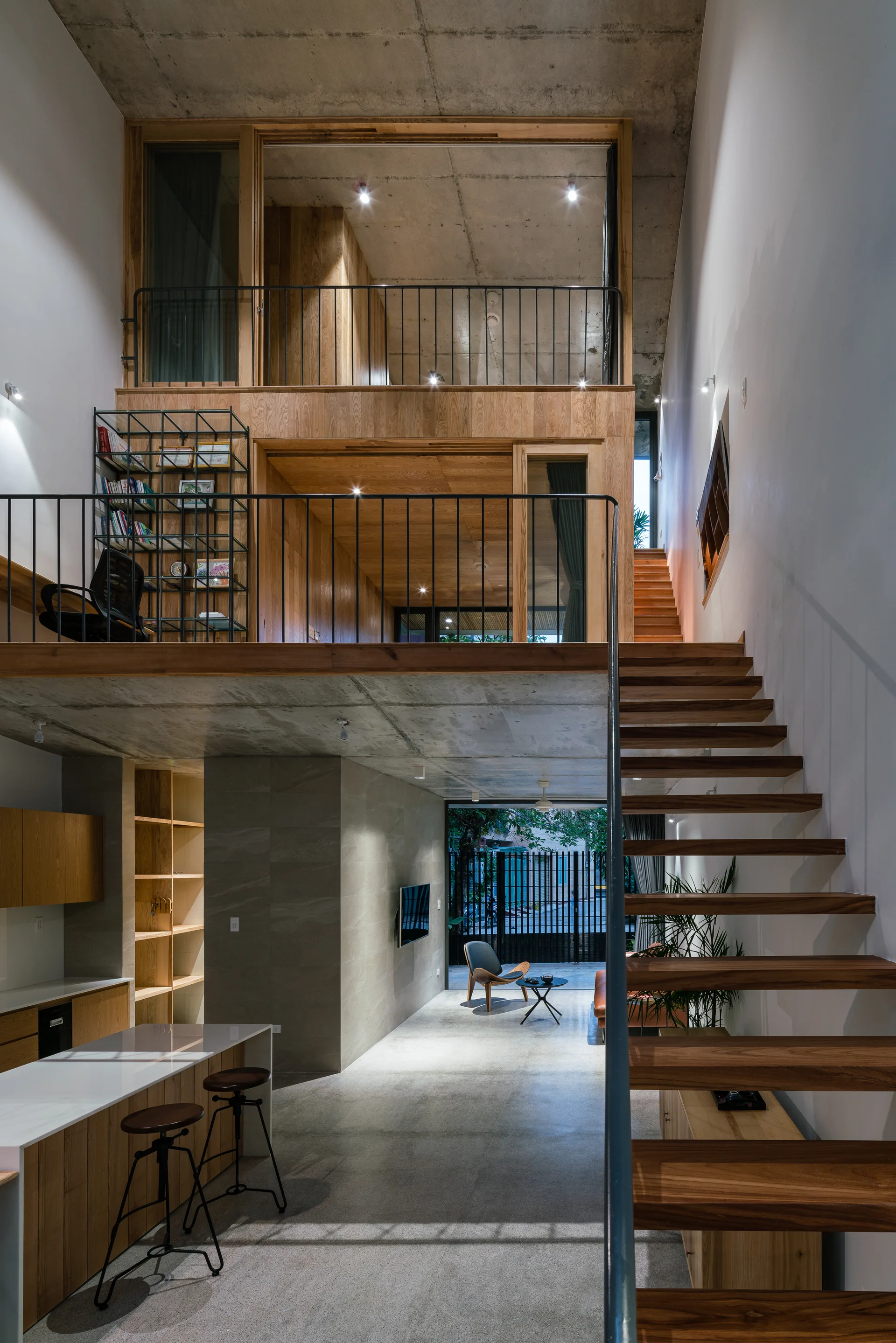 A multi-level interior features a floating wooden staircase, concrete ceilings, and two wood-paneled mezzanine levels with black metal railings.