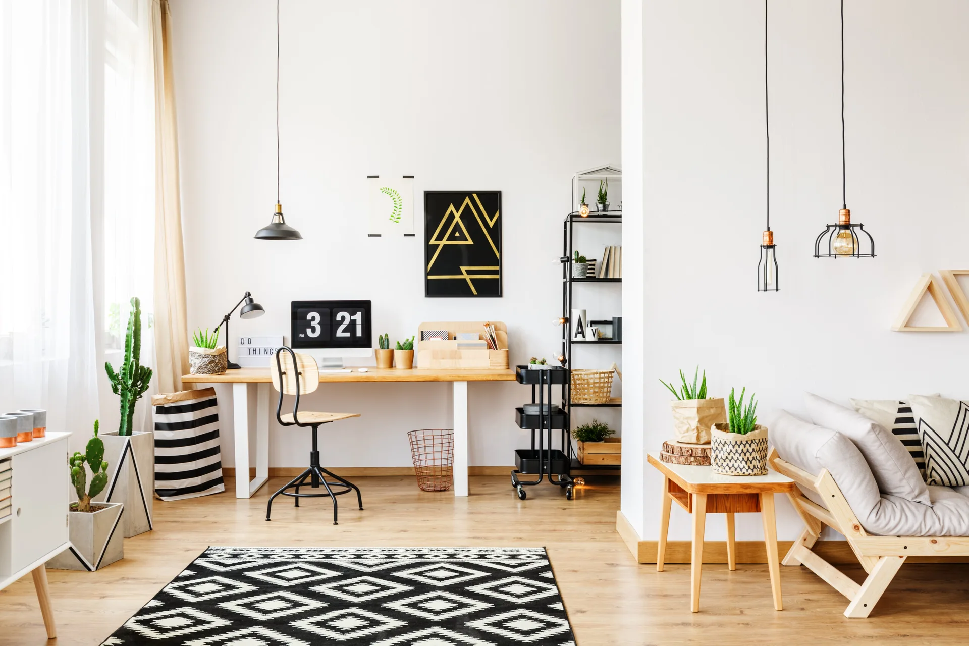 A Scandinavian home office features a wooden desk with a computer, a black metal rolling cart, and a bold geometric black and white rug on wood floors.