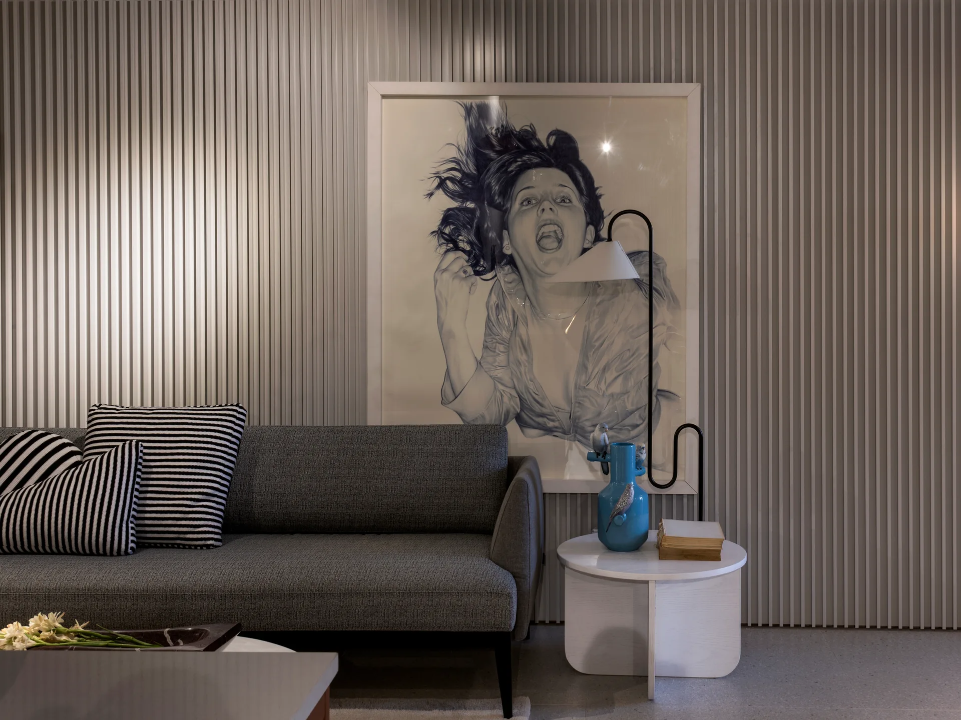 A grey fabric sofa with black-and-white striped pillows sits against a grey slatted wood feature wall displaying a large framed drawing.