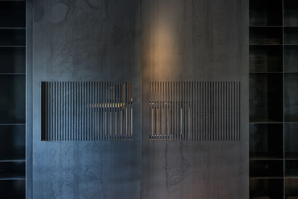 A dark charcoal textured wall cabinet system with a central slatted screen glowing with warm interior accent light next to open side shelves.