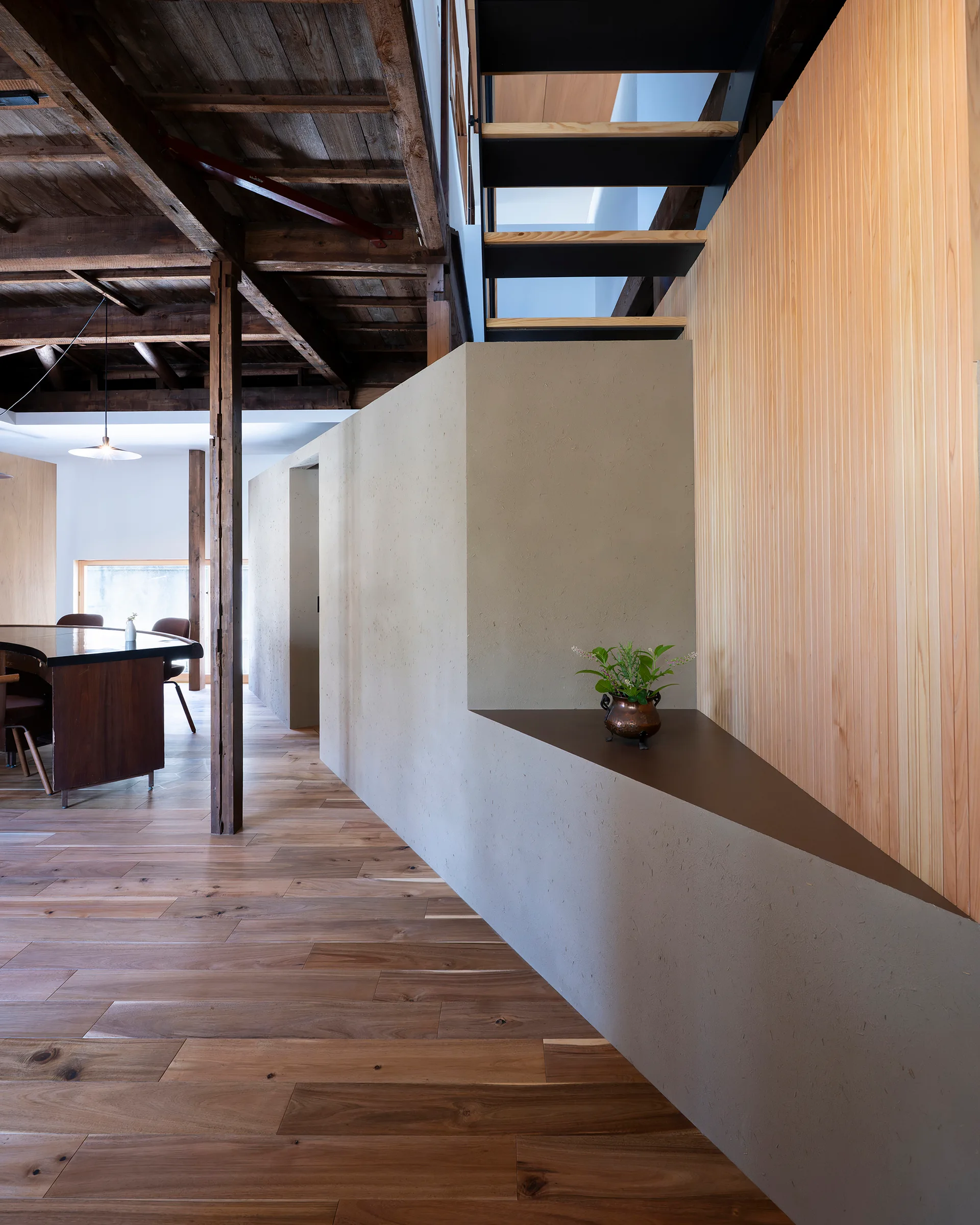 A modern staircase with black metal framing stands next to a vertical wood slat wall and a textured plaster partition with an angular display cutout.