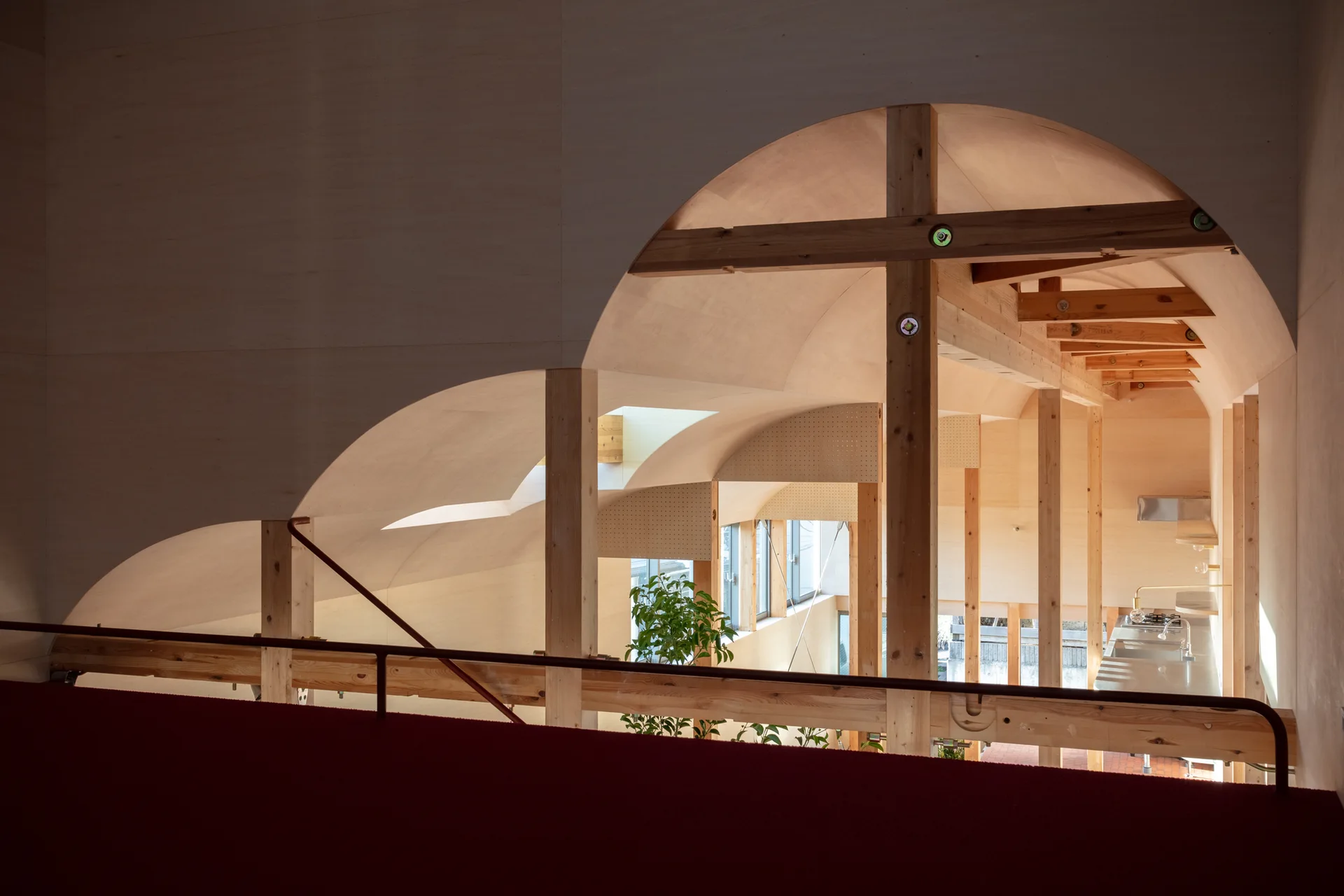 An overhead view from a loft shows a modern residential interior featuring curved plywood vaulted ceilings, exposed timber posts, and a bright atrium.