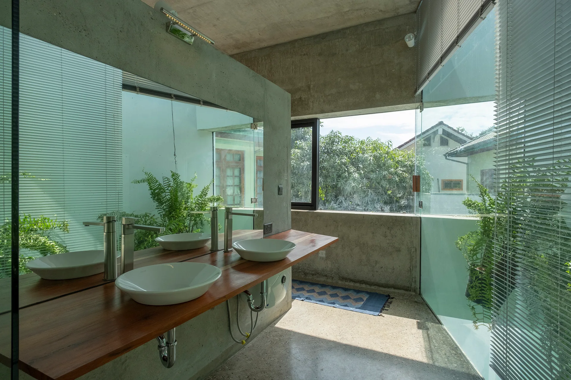 A modern concrete bathroom featuring a floating wood vanity with dual white vessel sinks, a large wall mirror, and floor-to-ceiling windows.