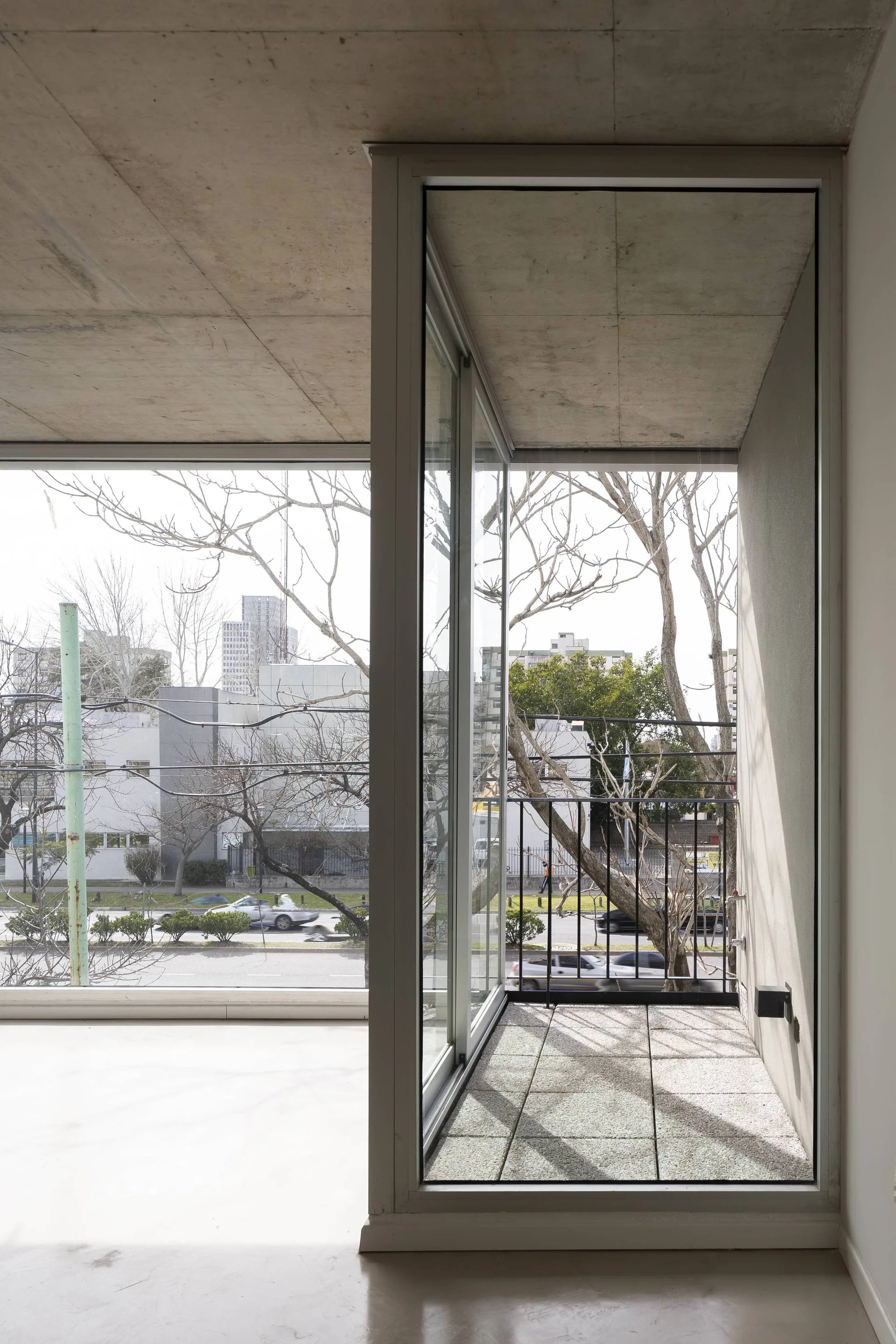 A sliding glass door opens to a small balcony with stone pavers and a black railing under an exposed concrete ceiling.