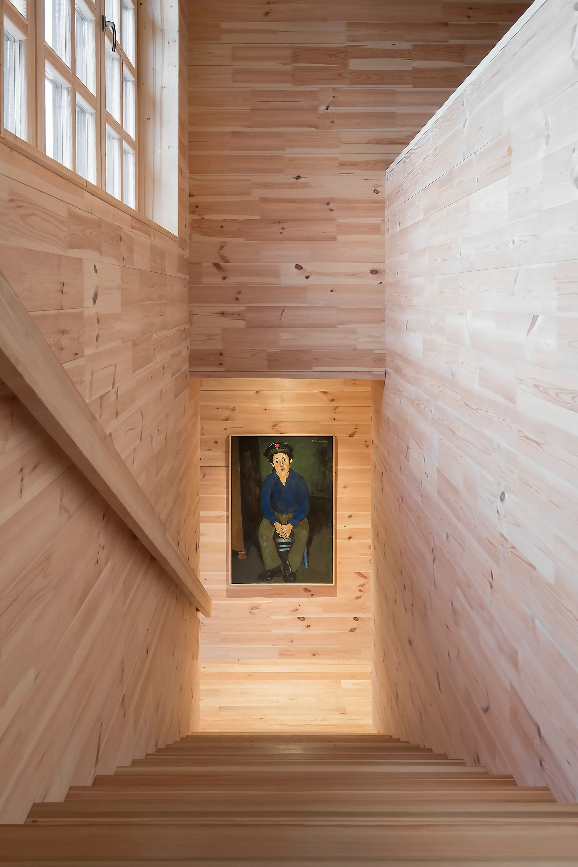 A wooden staircase descends between walls clad in light horizontal wood planks, with a framed portrait painting hanging on the landing wall.