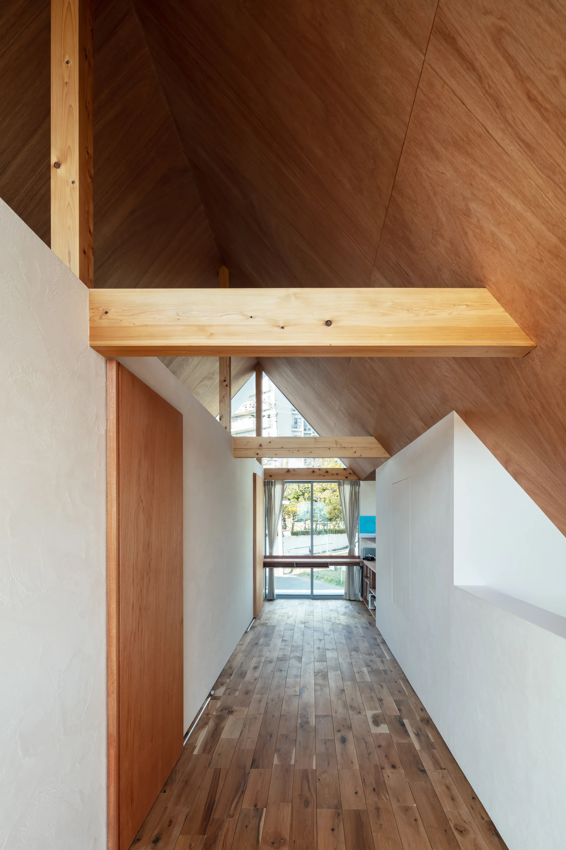 A long interior hallway features white walls, medium-brown wood flooring, and a high vaulted wood ceiling with exposed structural beams.