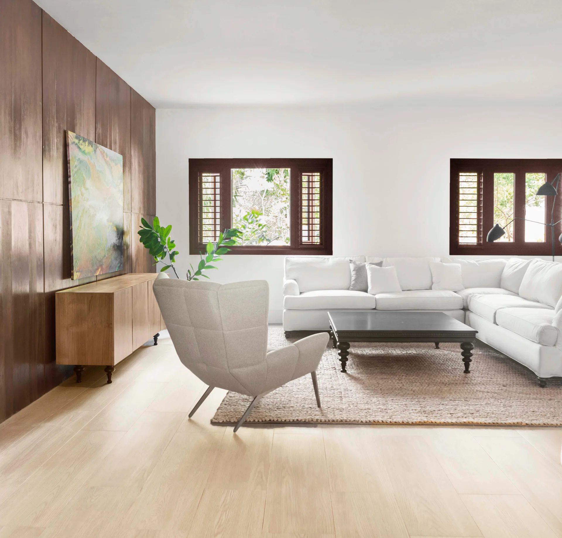 A bright living room features a white sectional sofa, a dark wood coffee table, a light wood floor, and a dark wood paneled accent wall.